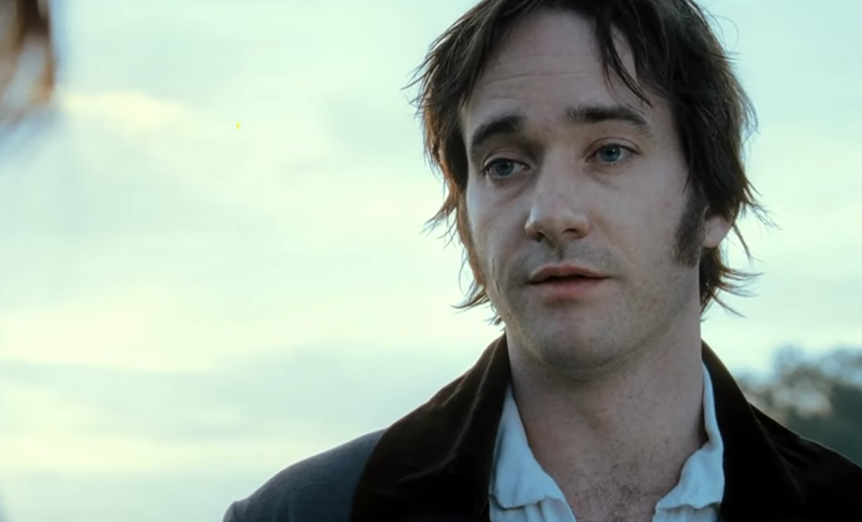 Matthew Macfadyen as Mr. Darcy standing outdoors with a neutral expression