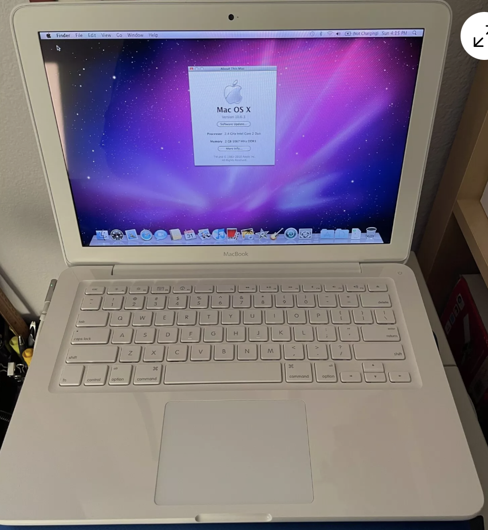 A white MacBook laptop with a garden image as its wallpaper. The garden features a variety of flowers in full bloom. The laptop is on a lace-covered table