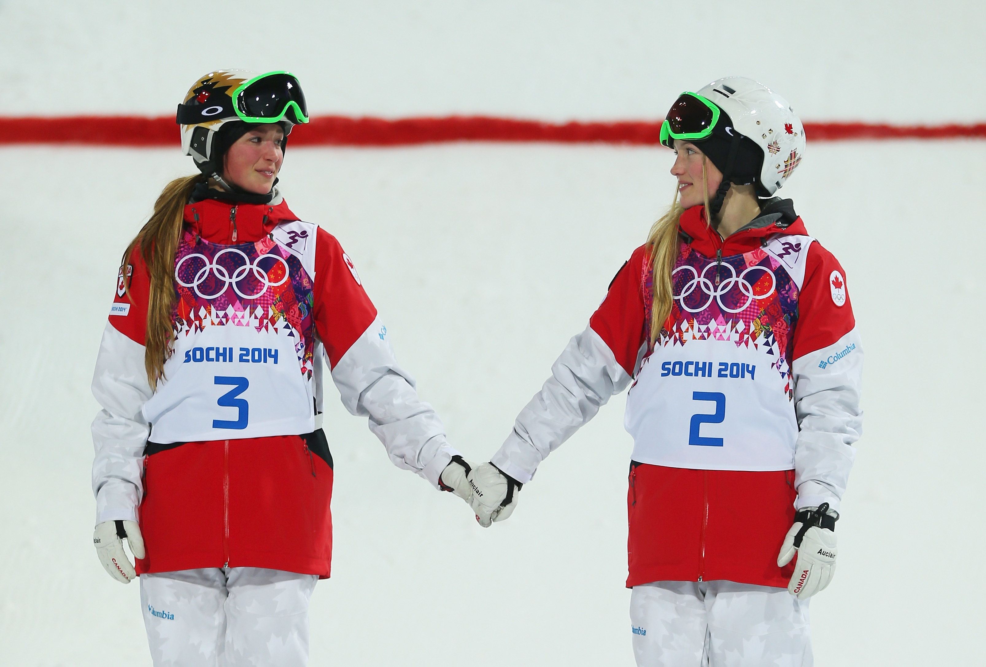 Skier No. 3 and Skier No. 2 holding hands, wearing Sochi 2014 Olympic gear, standing on a snowy field