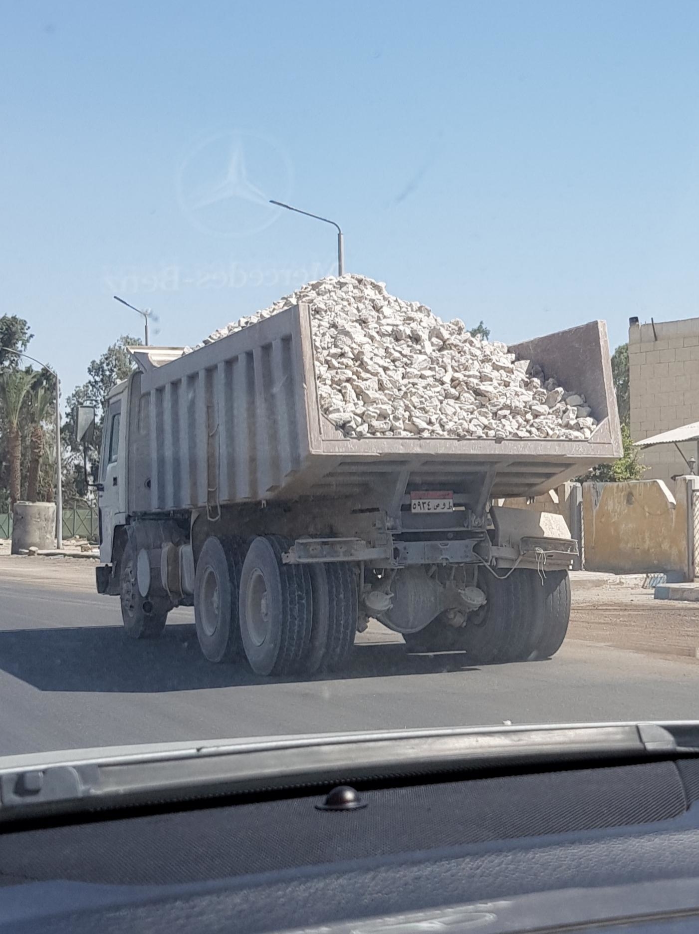 A dump truck loaded with rocks driving down a road seen from the inside of another vehicle
