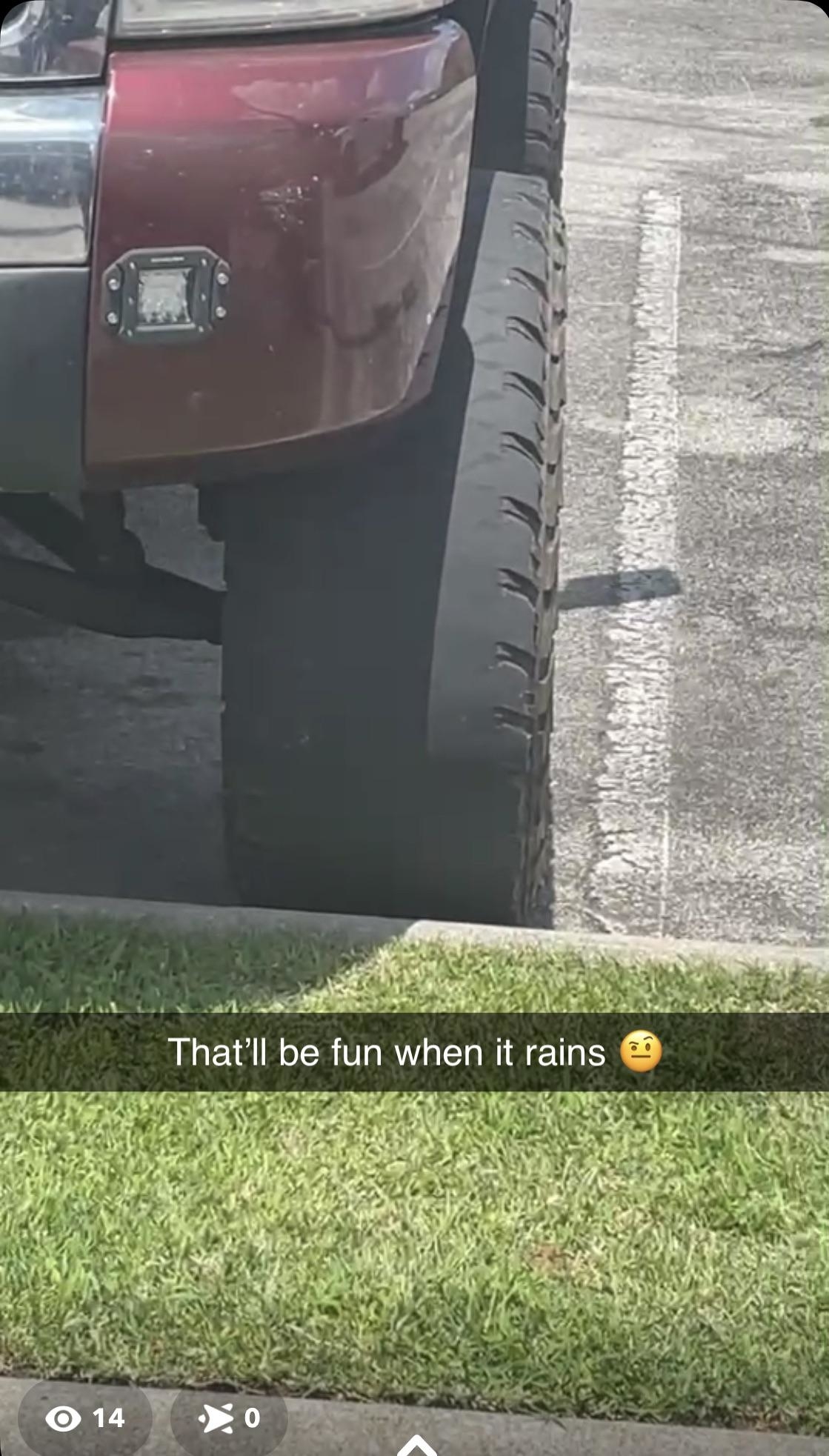 Close-up of a large truck tire with a Snapchat caption reading, "That’ll be fun when it rains ?." The tire is parked next to a grassy area
