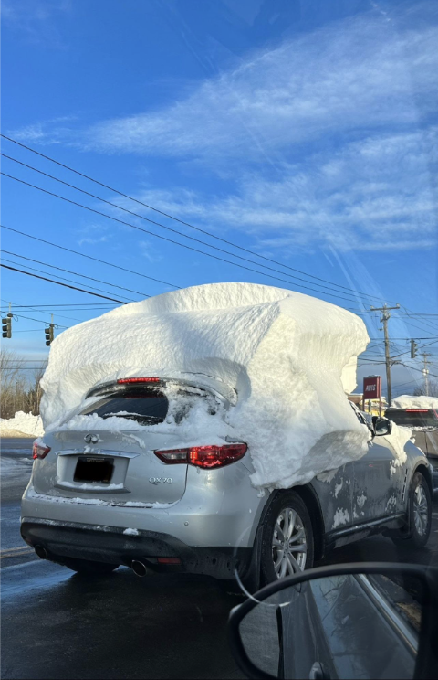 Car with a large amount of snow accumulated on the roof and rear windshield, driving on a sunny day