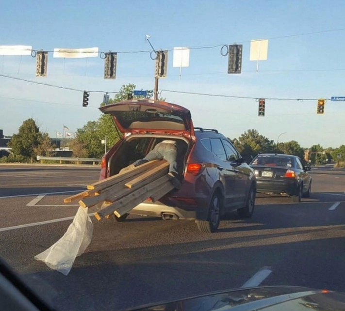 Open SUV driving on a road with its trunk open, carrying several large wooden beams that extend out the back