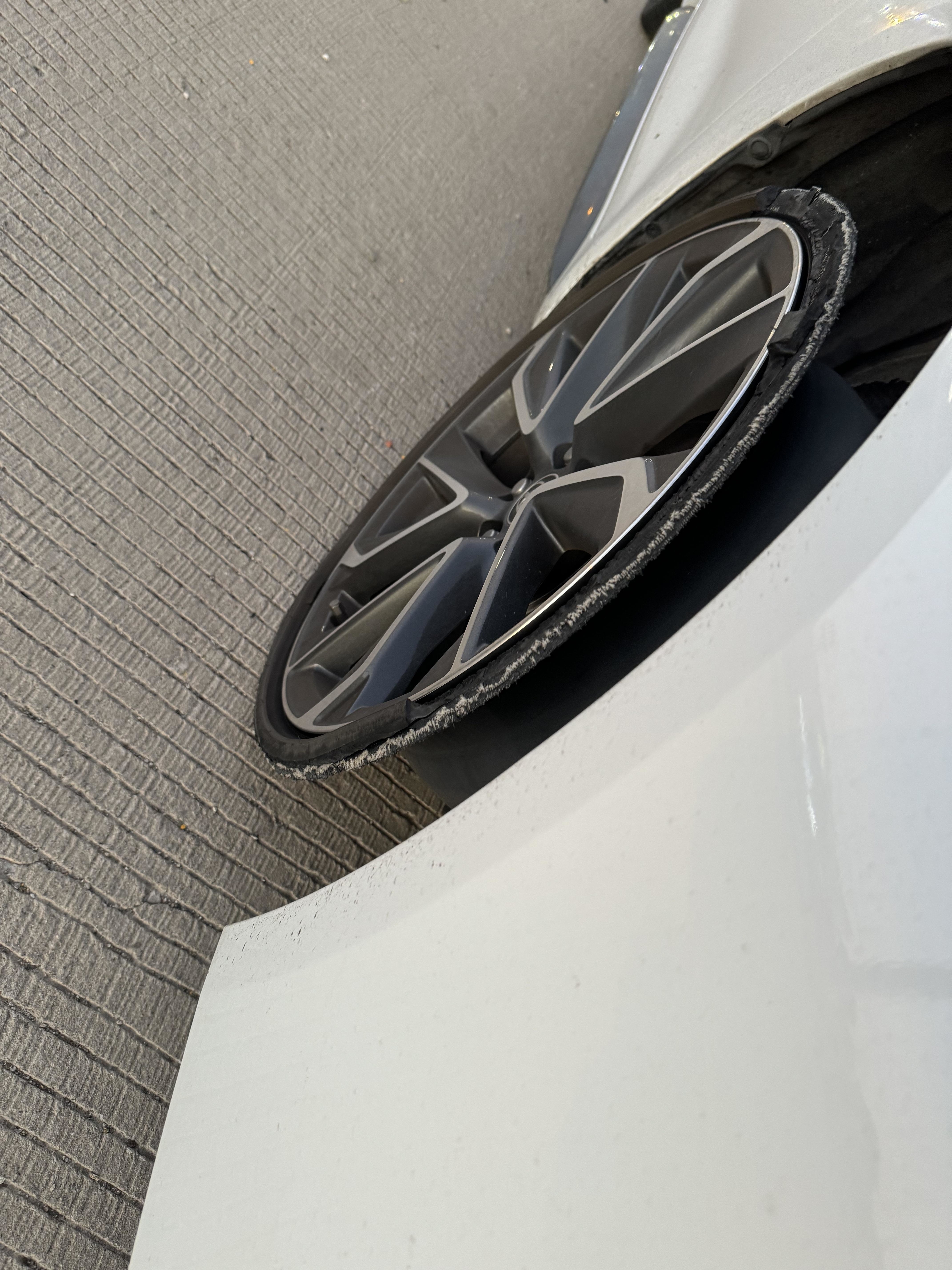 A close-up of a damaged car wheel and its rim, positioned at an abnormal angle against the road surface, indicating potential vehicle damage