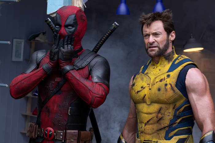 Ryan Reynolds as Deadpool in his red and black suit and Hugh Jackman as Wolverine in a yellow and blue suit stand together, both looking surprised