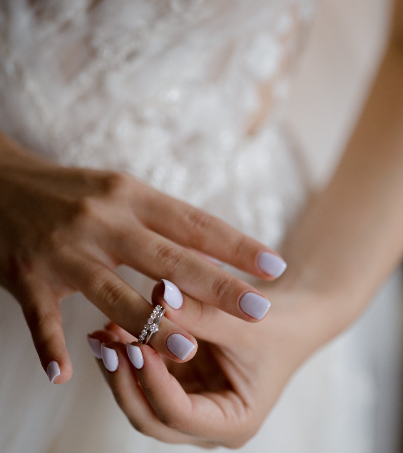 Person in a wedding dress showing off an engagement ring and manicured hands