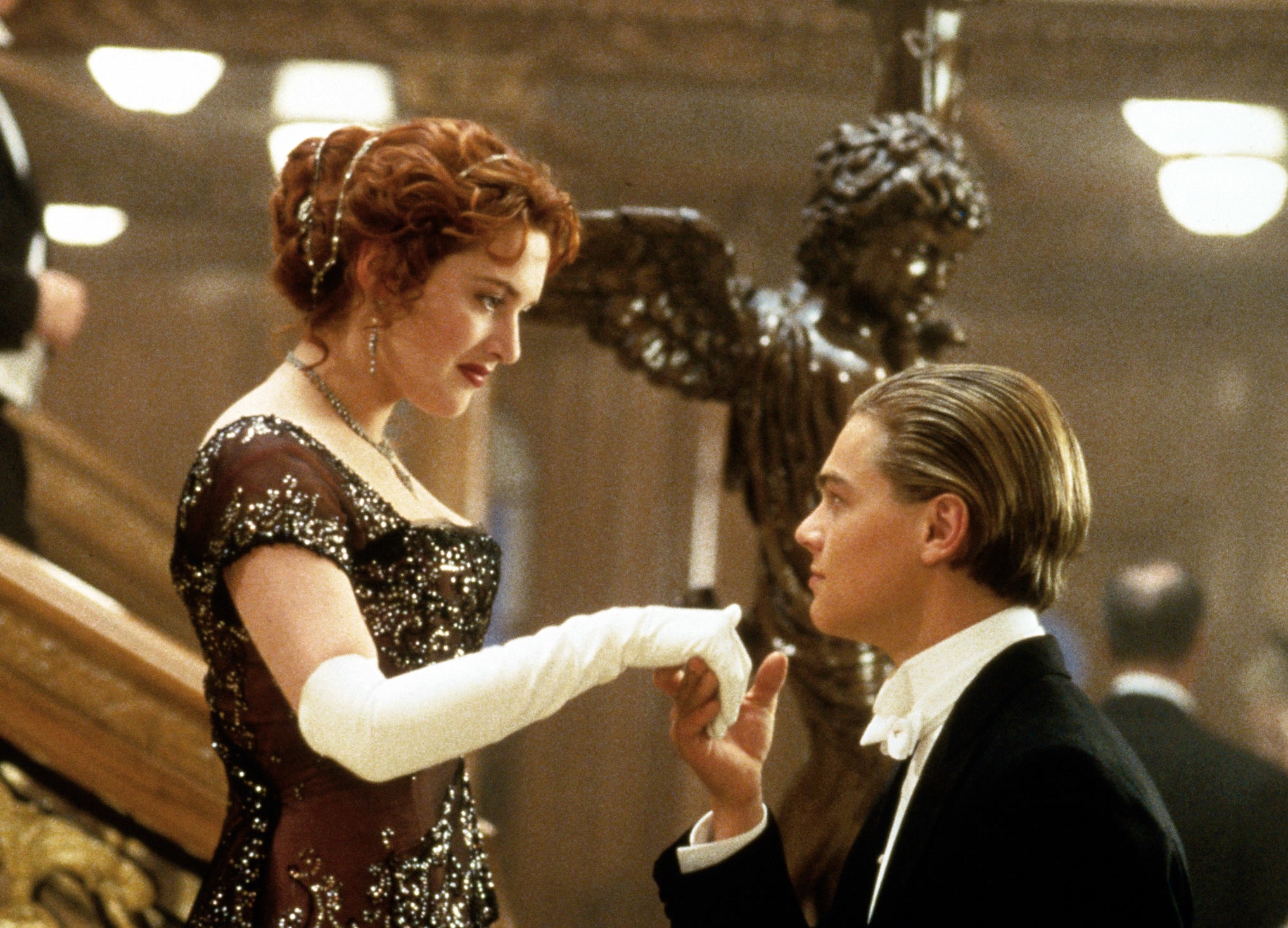 Kate Winslet in an elegant lace gown and Leonardo DiCaprio in a tuxedo share a romantic moment on a grand staircase