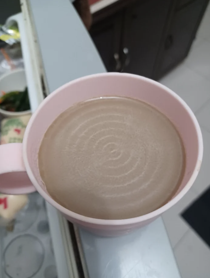 A cup of coffee with a rippled surface, indicating it has recently been stirred, is placed on a table in a home kitchen environment
