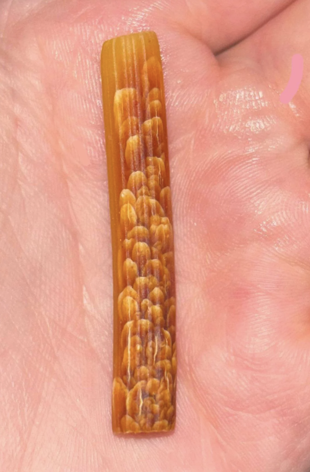A hand holding a unique, rectangular piece of jewelry featuring a textured, scaled design