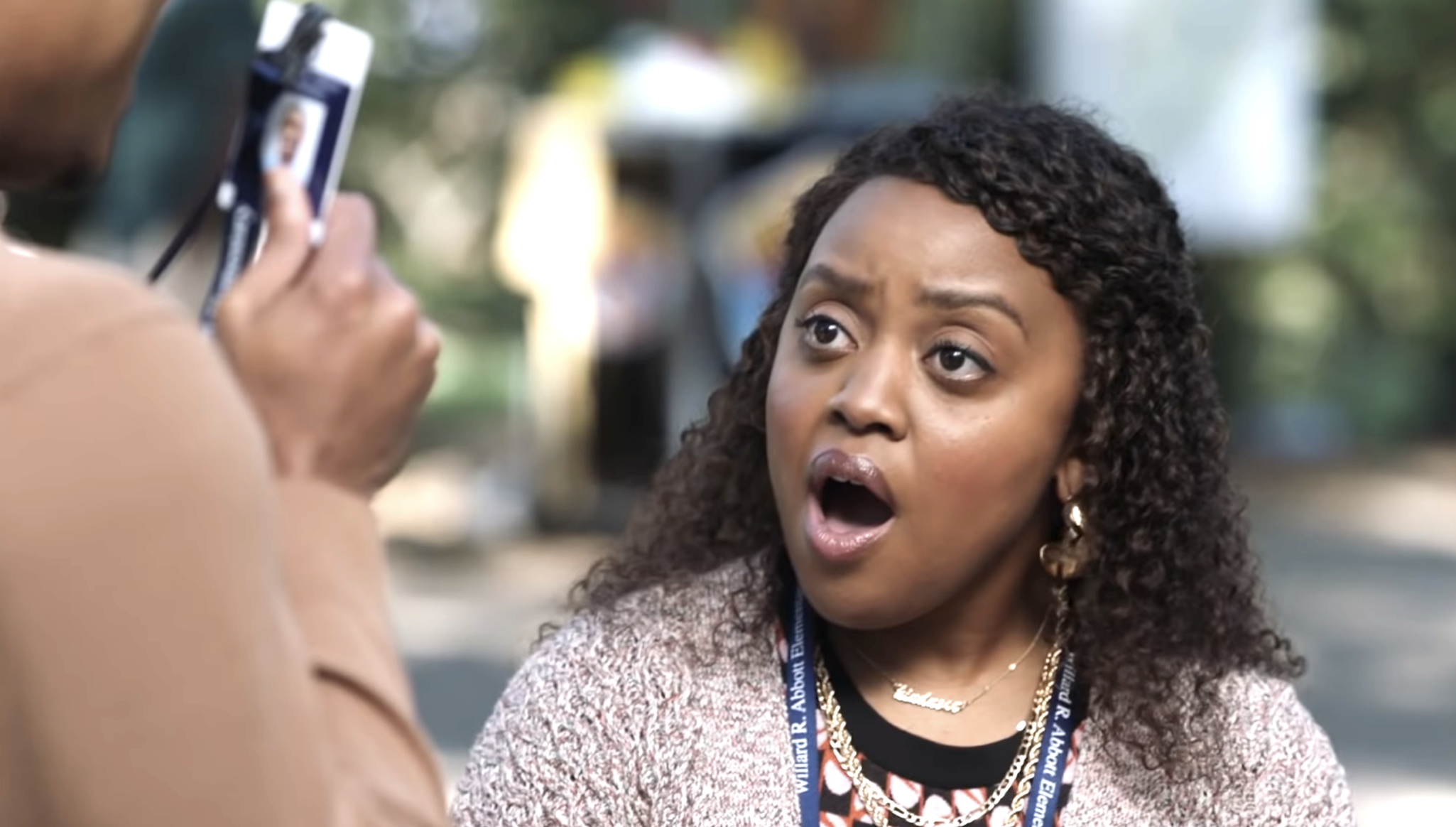 A woman with curly hair and a surprised expression is being photographed by another person outdoors