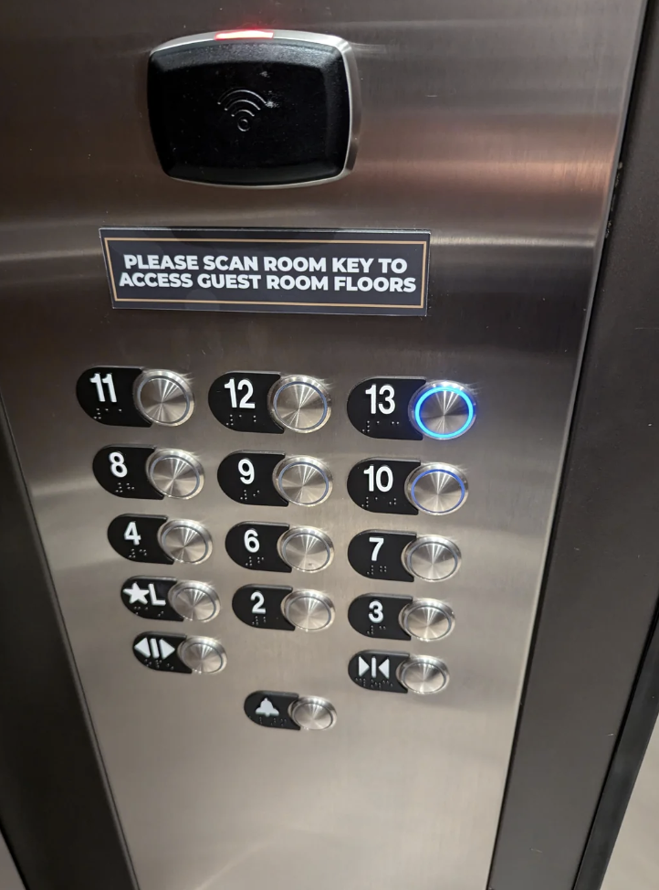 Elevator control panel with floors 1-13, emergency button, and a sign reading "Please scan room key to access guest room floors."
