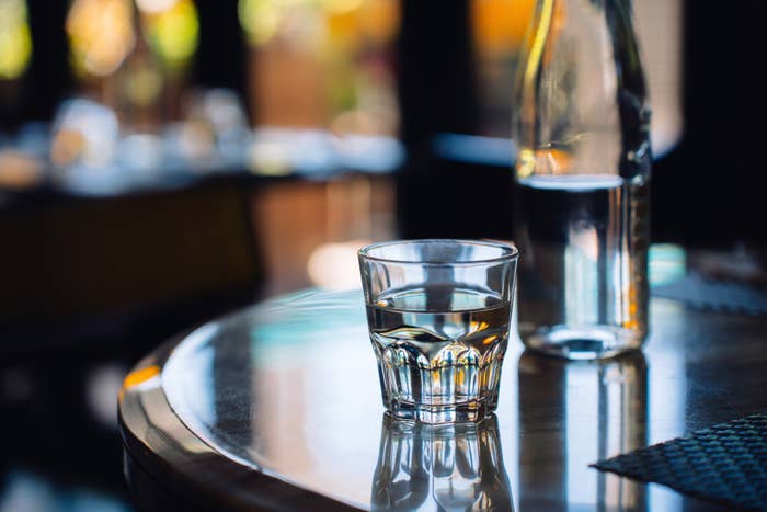 A clear glass of water and a water bottle on a polished wooden table indoors, with blurred background elements