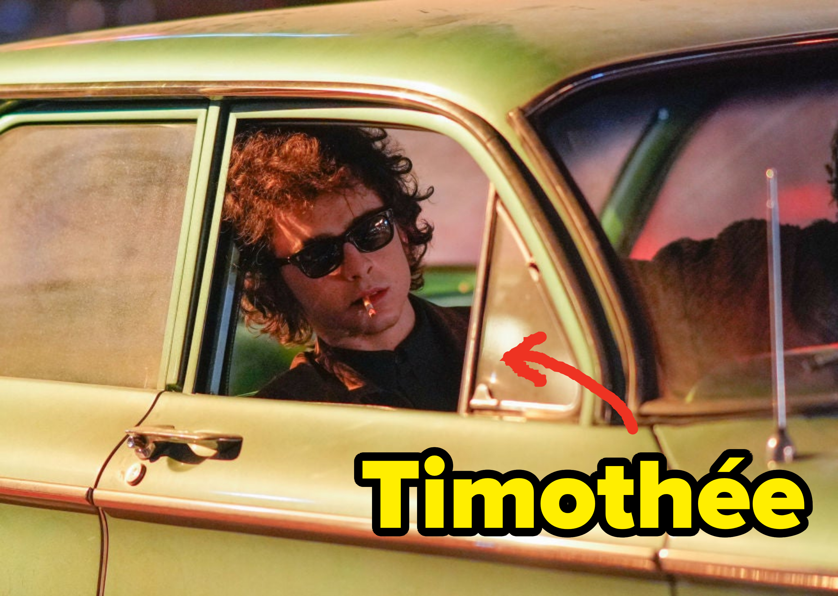 A person wearing dark sunglasses and a black outfit seated inside a car, looking out the window with a contemplative expression