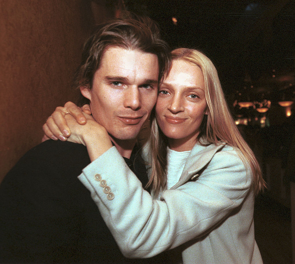 Ethan Hawke and Uma Thurman embrace, smiling at the camera. Ethan wears a dark jacket, while Uma wears a light-colored outfit