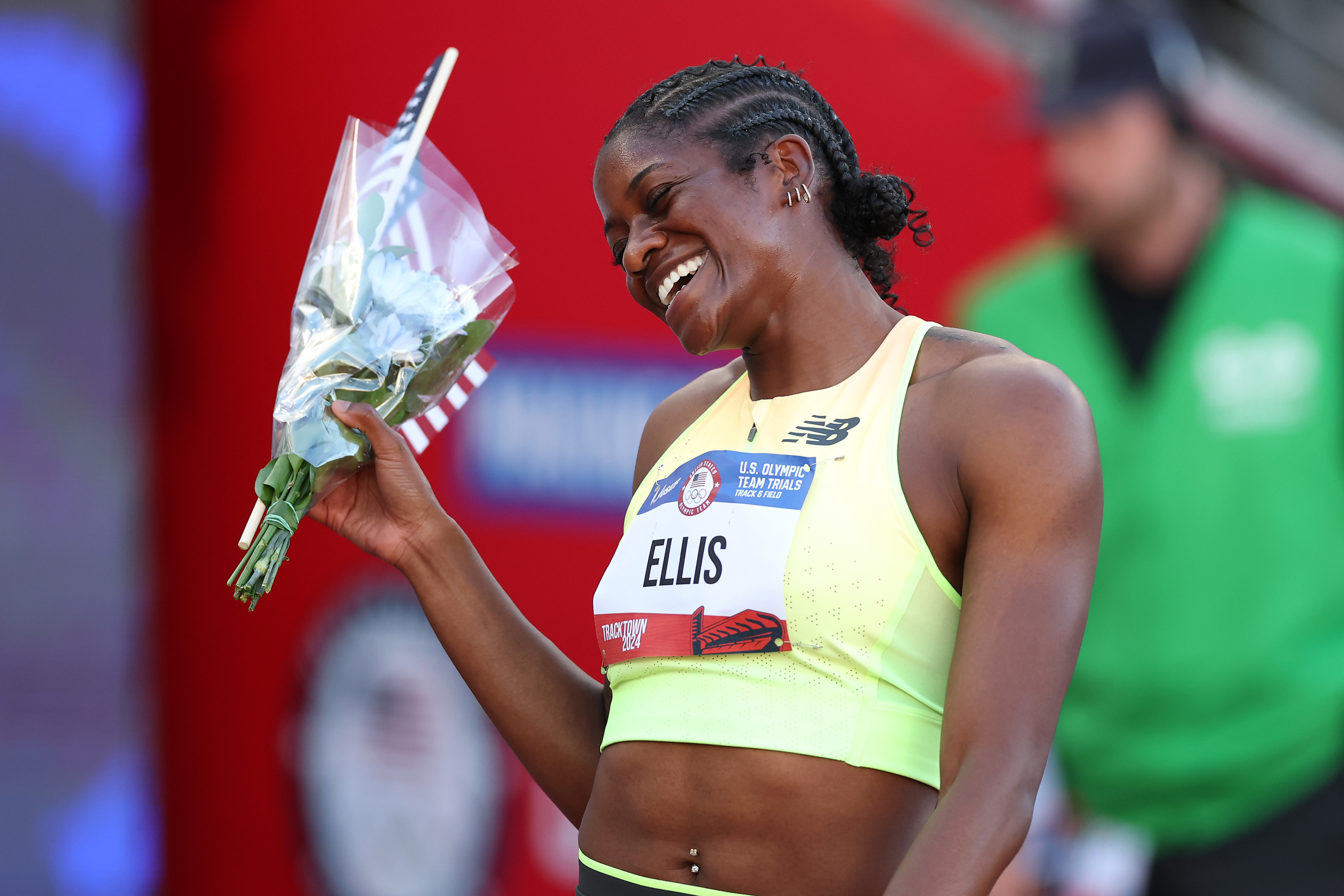 Track athlete Ellis smiles and holds a small bouquet of flowers while wearing a sports bra and bib with her name at the U.S. Olympic Team Trials venue