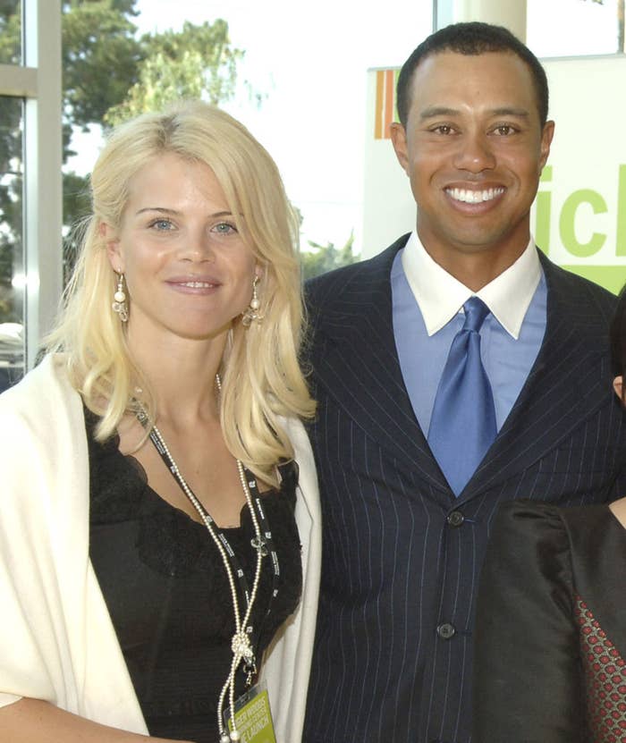 Tiger Woods and Elin Nordegren are posing together. Tiger is wearing a pinstripe suit and blue tie, while Elin is in a black dress and white shawl