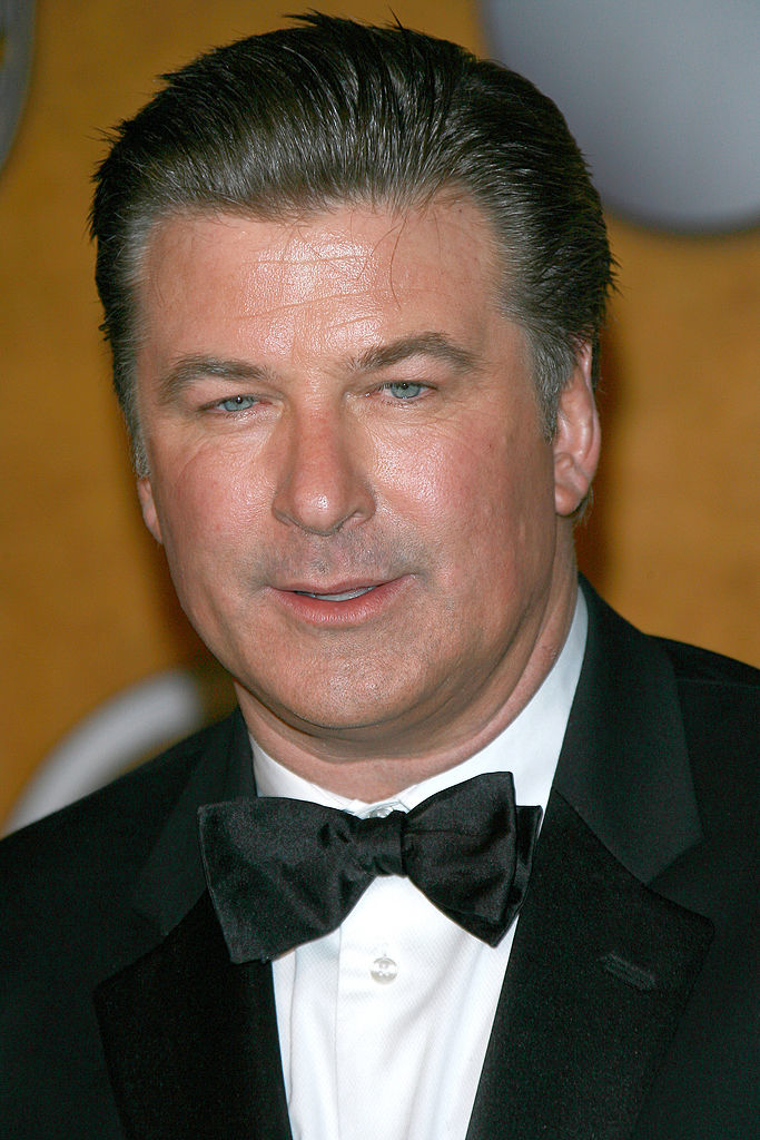 Alec Baldwin, dressed in a classic black tuxedo with a black bow tie, poses for a photo at a formal event