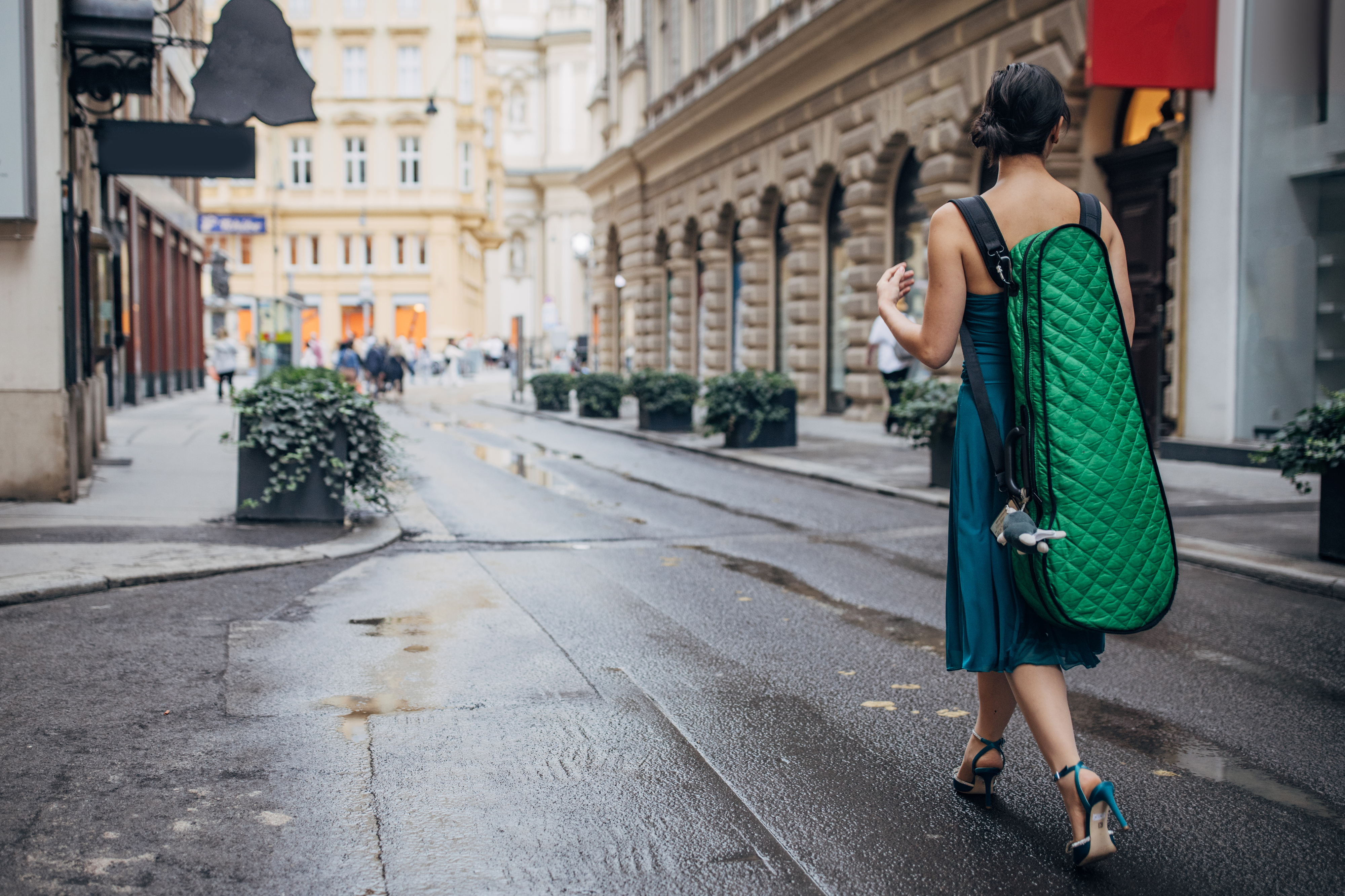 A woman in a blue dress walks down a city street with a large green quilted item strapped to her back