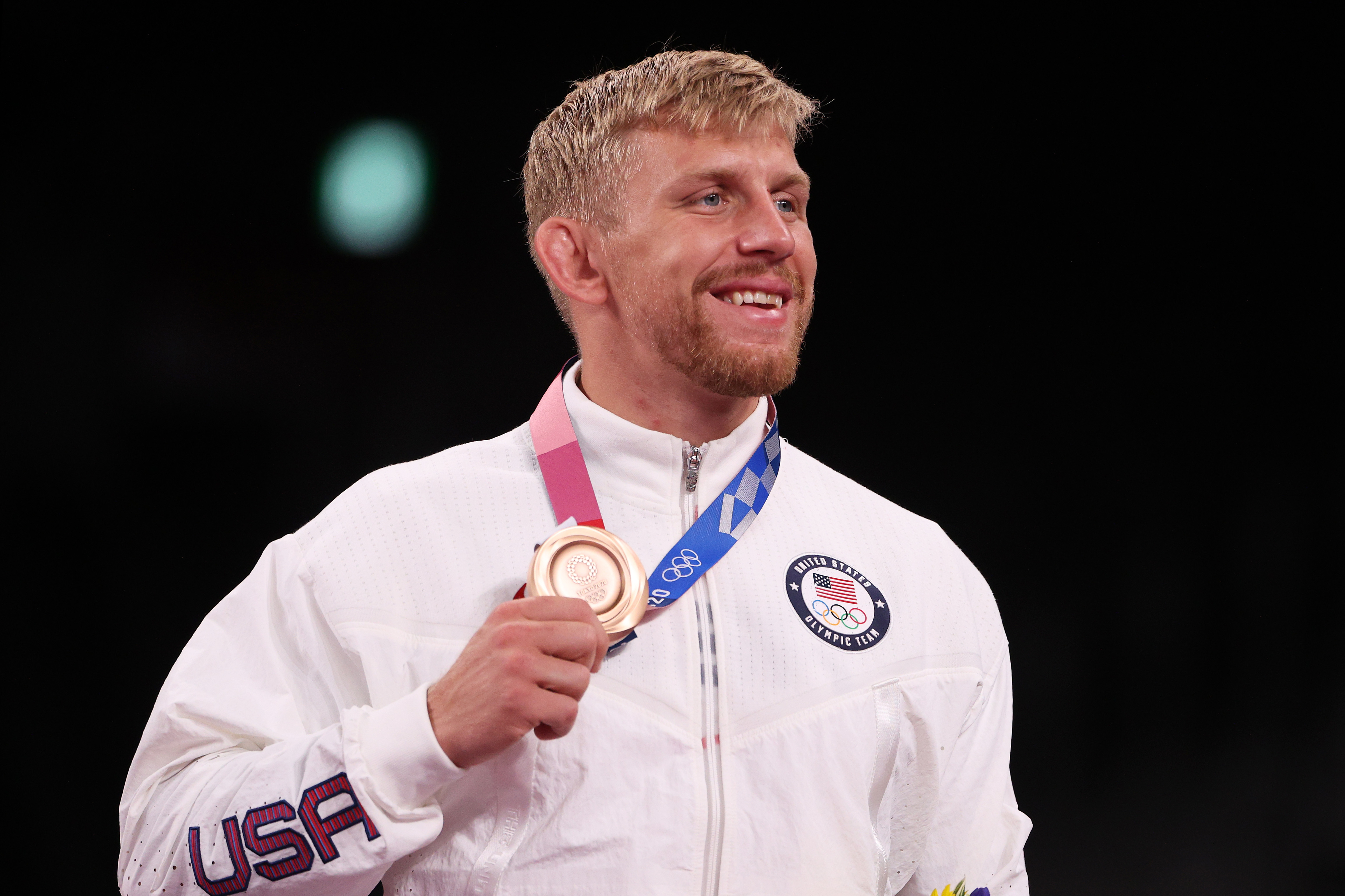 Athlete holding a bronze medal with a smile, dressed in a sports jacket with the &quot;USA&quot; emblem. Image is associated with sports news