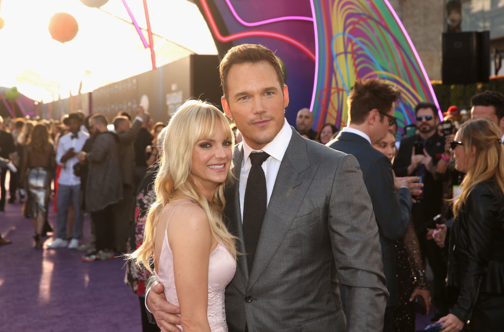 Anna Faris and Chris Pratt pose together on the red carpet. Anna wears a sleeveless gown, Chris wears a suit and tie. Crowd and colorful backdrop behind them