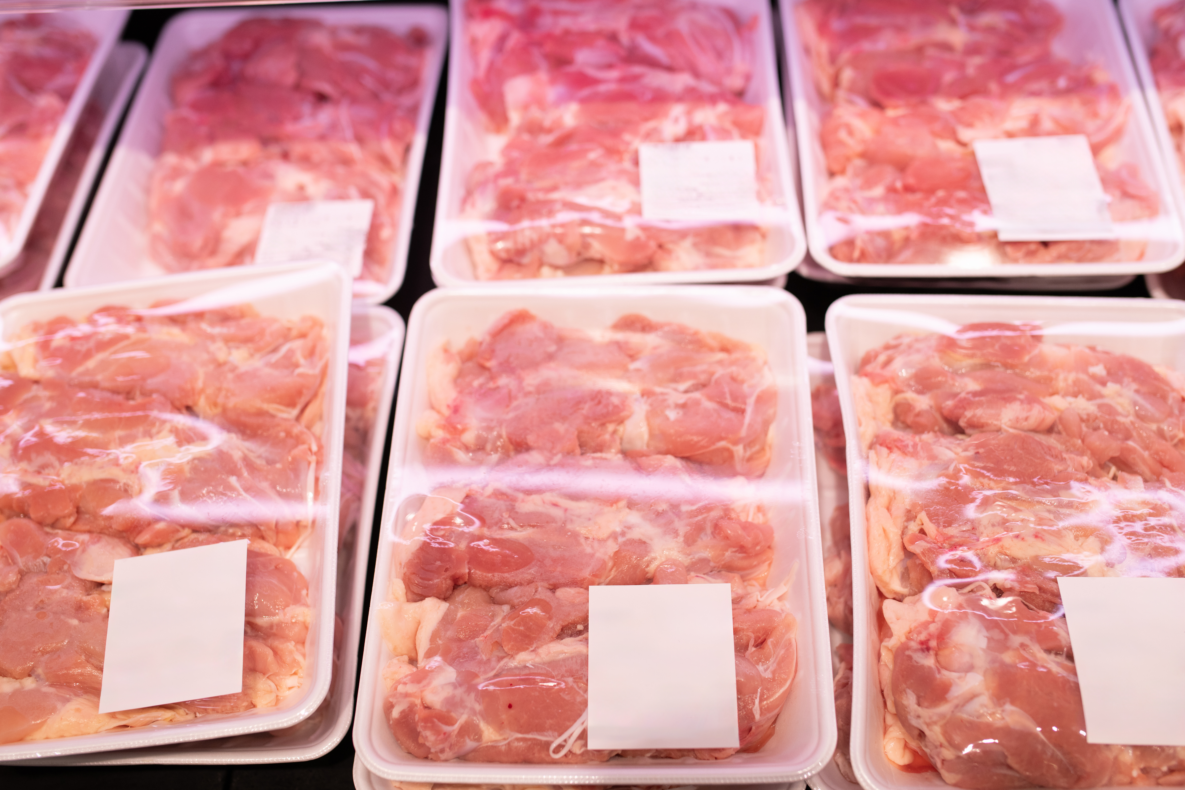 Multiple packages of raw poultry, with white labels, are displayed in a grocery store's refrigerated section