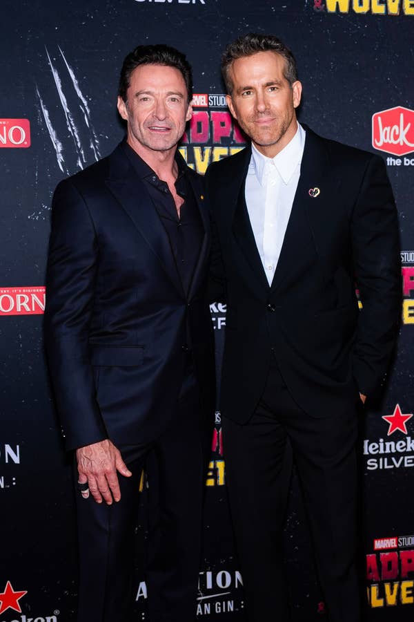 Hugh Jackman and Ryan Reynolds pose in suits at the &quot;Deadpool 3&quot; event. Hugh wears a dark suit, while Ryan dons a black suit with a white shirt