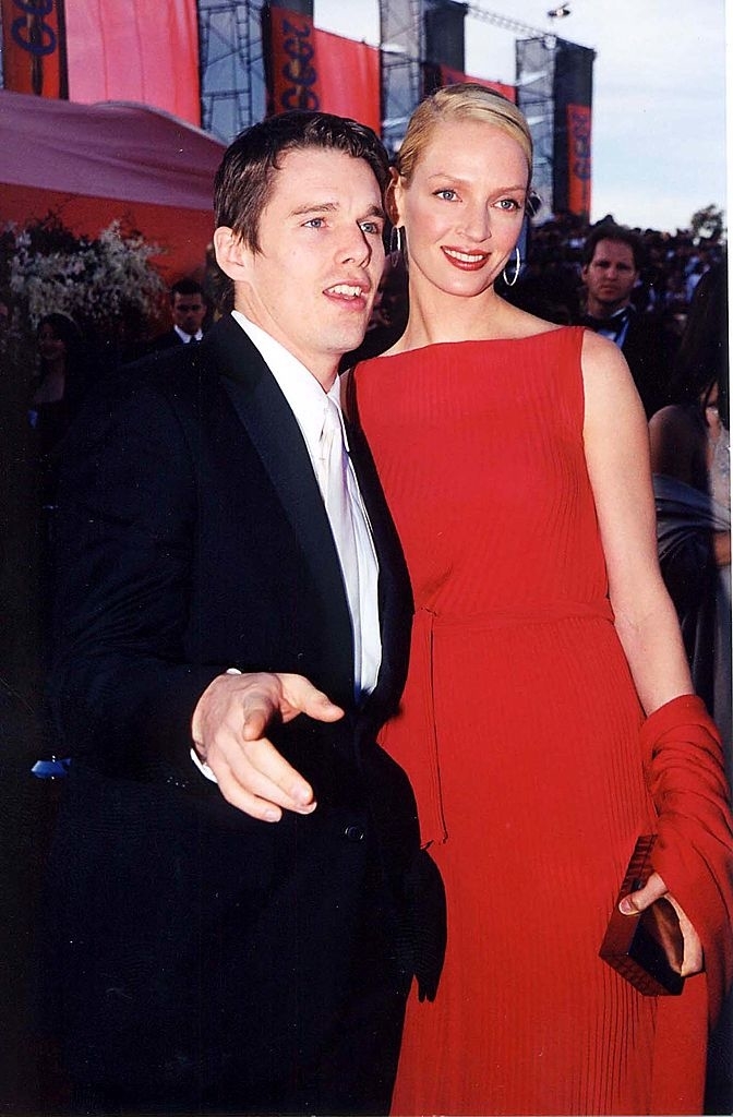 Ethan Hawke in a black suit and Uma Thurman in a sleeveless, elegant dress pose on the red carpet at a formal event