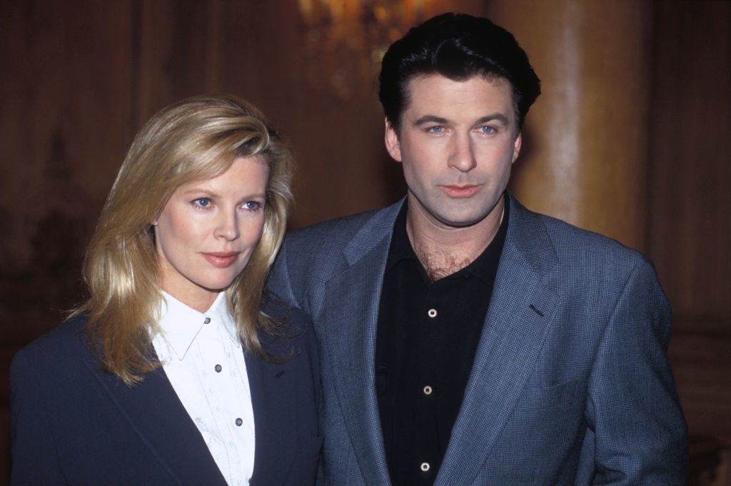 Kim Basinger and Alec Baldwin stand together, with Kim wearing a dress shirt and blazer, and Alec wearing a dress shirt and blazer