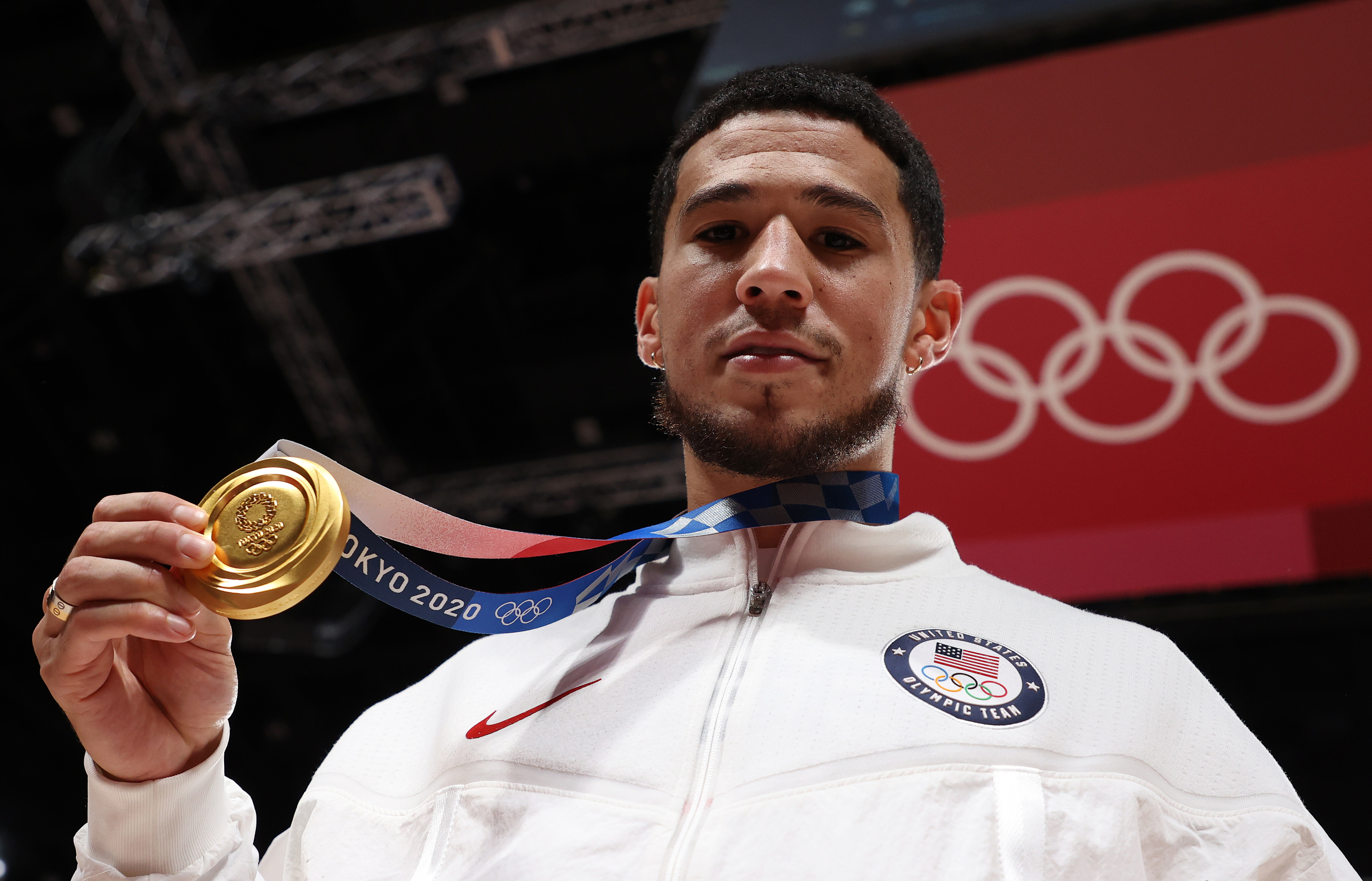 Devin Booker holds up his gold medal while wearing a white Team USA tracksuit at the Tokyo 2020 Olympics