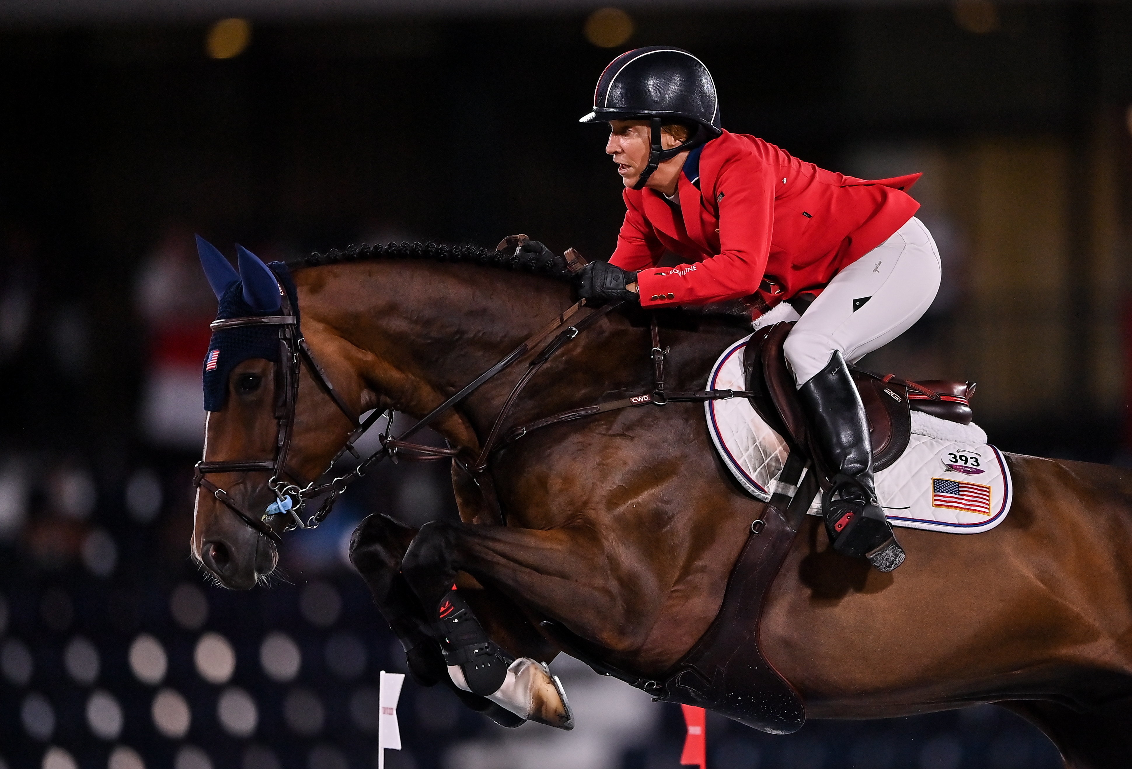 Equestrian rider Laura Kraut  in red jacket and white pants jumps with horse over hurdle in a sports competition