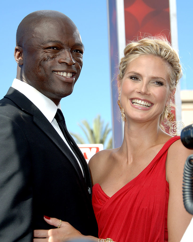 Heidi Klum in an elegant one-shoulder dress and Seal in a suit, smiling together at an event