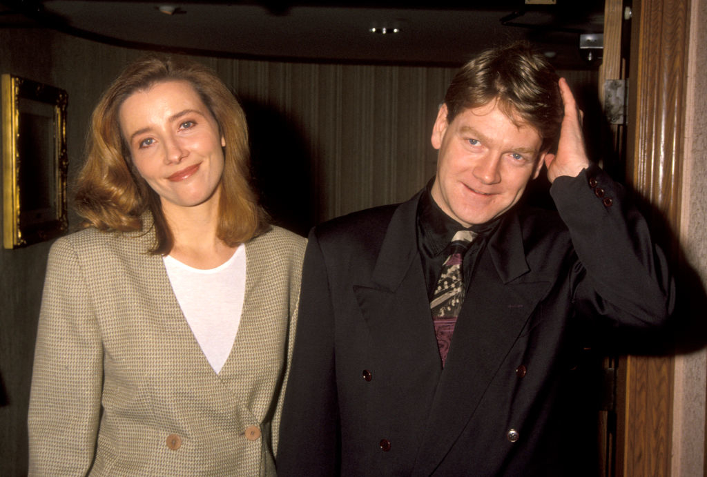 A woman and a man, both smiling, stand together; the woman wears a light blazer and the man wears a dark suit with a patterned tie