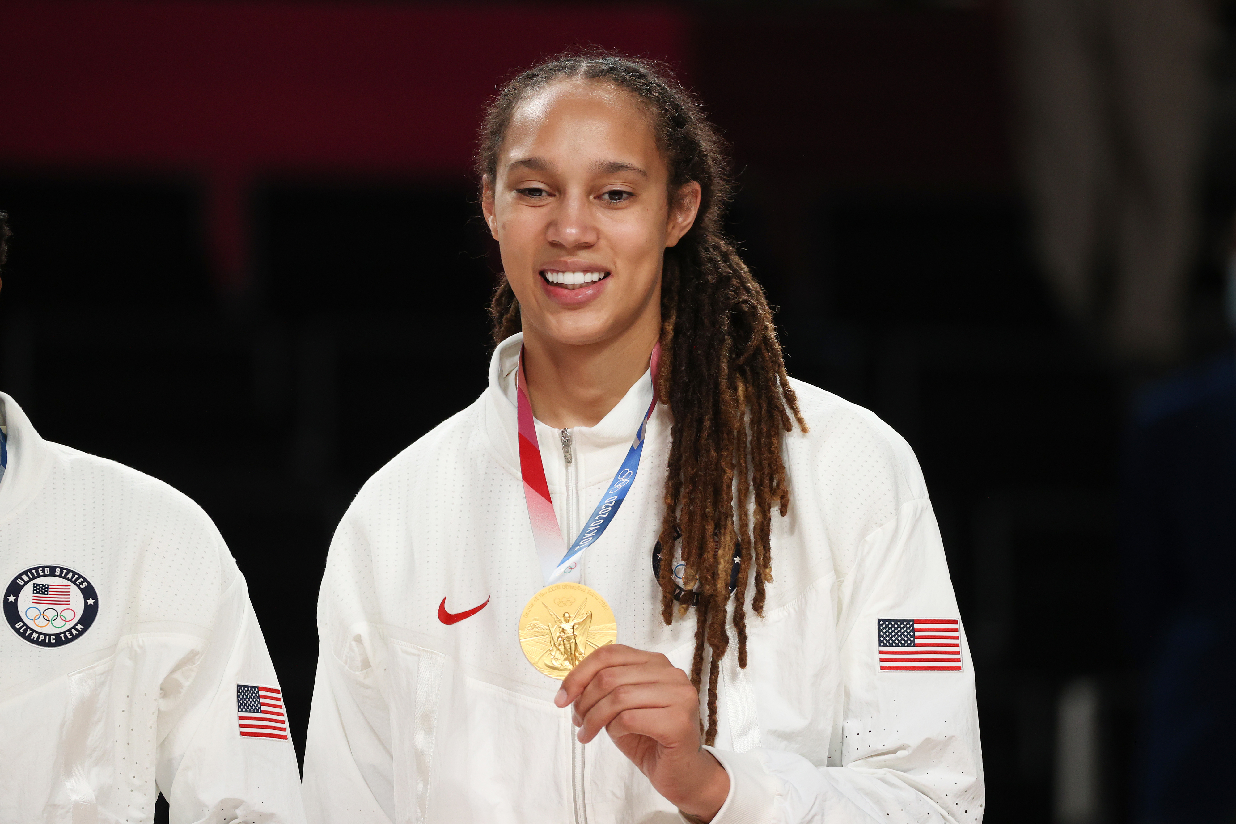 Brittney Griner smiles while holding a gold medal, wearing a USA Team jacket