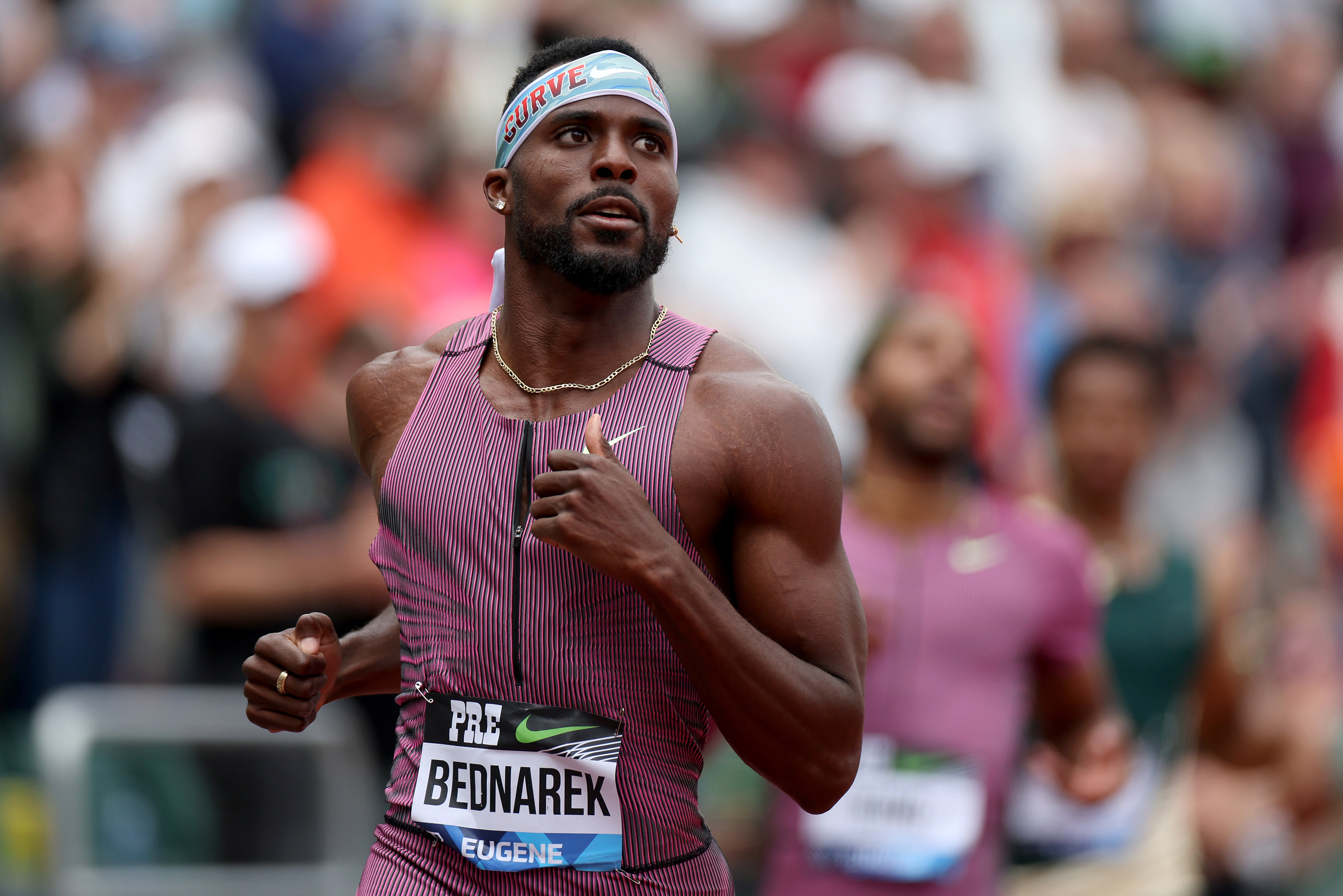 Kenny Bednarek running during a track event, wearing a headband and athletic gear