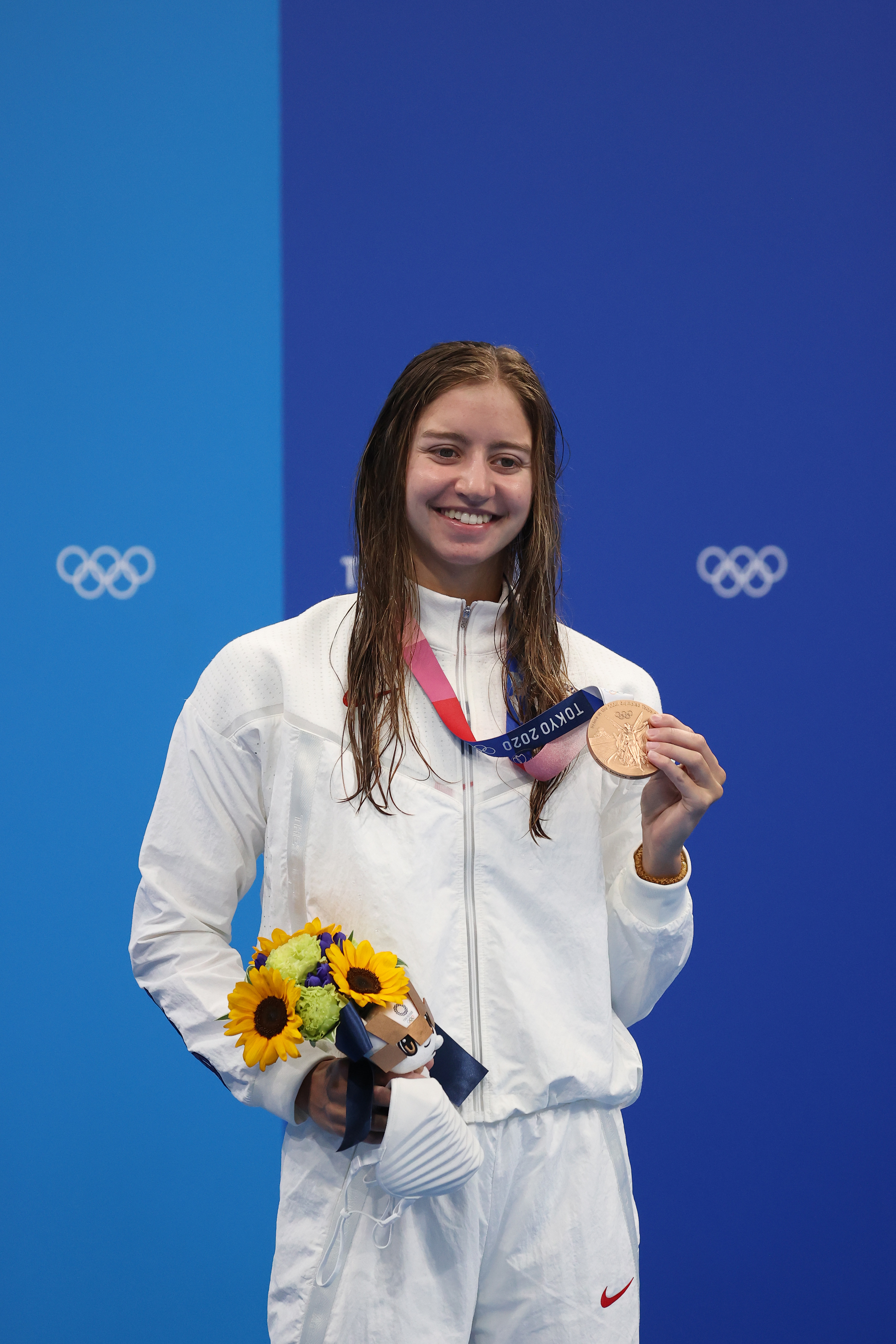 Kate Douglass stands smiling, holding a bronze medal and a bouquet of flowers during the Tokyo 2020 Olympics