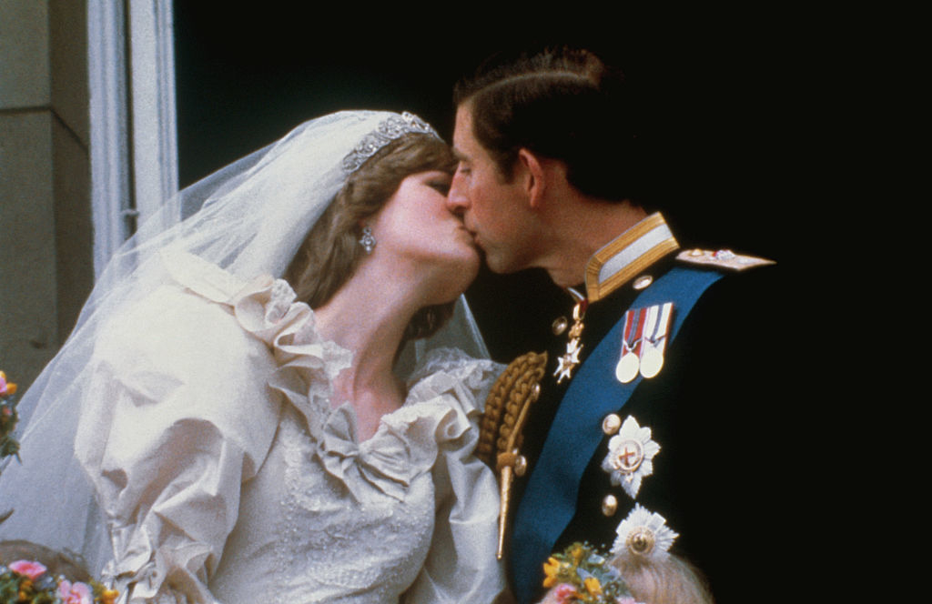 Princess Diana in an elegant wedding gown and Prince Charles in formal military attire, share a kiss on a balcony after their wedding ceremony