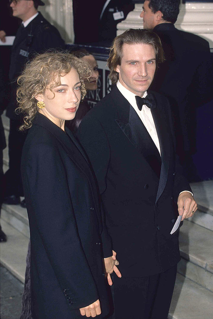 Alex Kingston and Ralph Fiennes, dressed in elegant black formal wear, stand together at a formal event