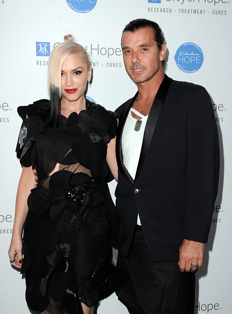 Gwen Stefani and Gavin Rossdale pose together at a City of Hope charity event. Gwen is wearing a black, sheer dress with floral patterns, and Gavin is in a black suit
