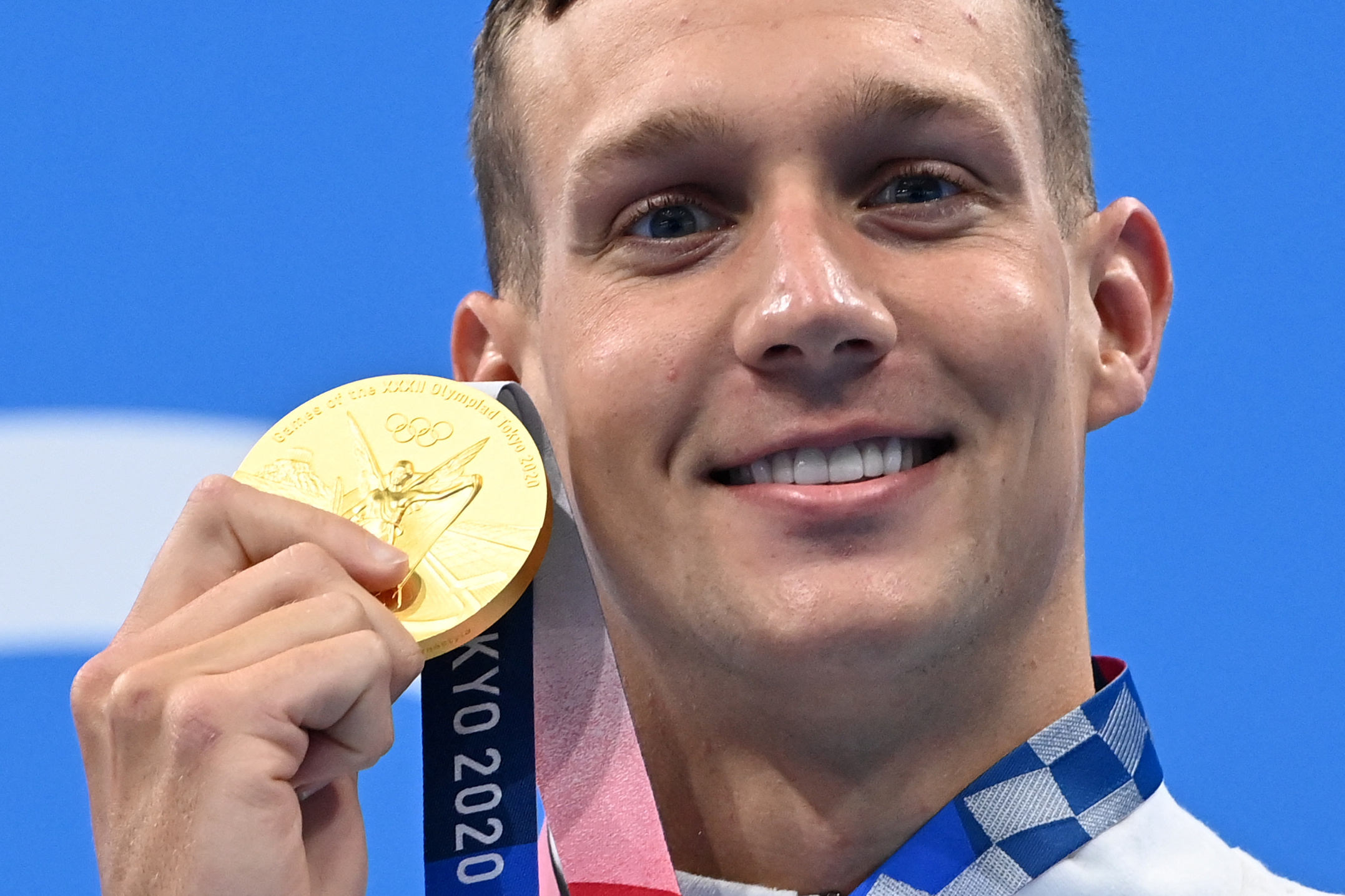 Caeleb Dressel holding his Olympic gold medal with a smile after winning at the Tokyo 2020 Olympics