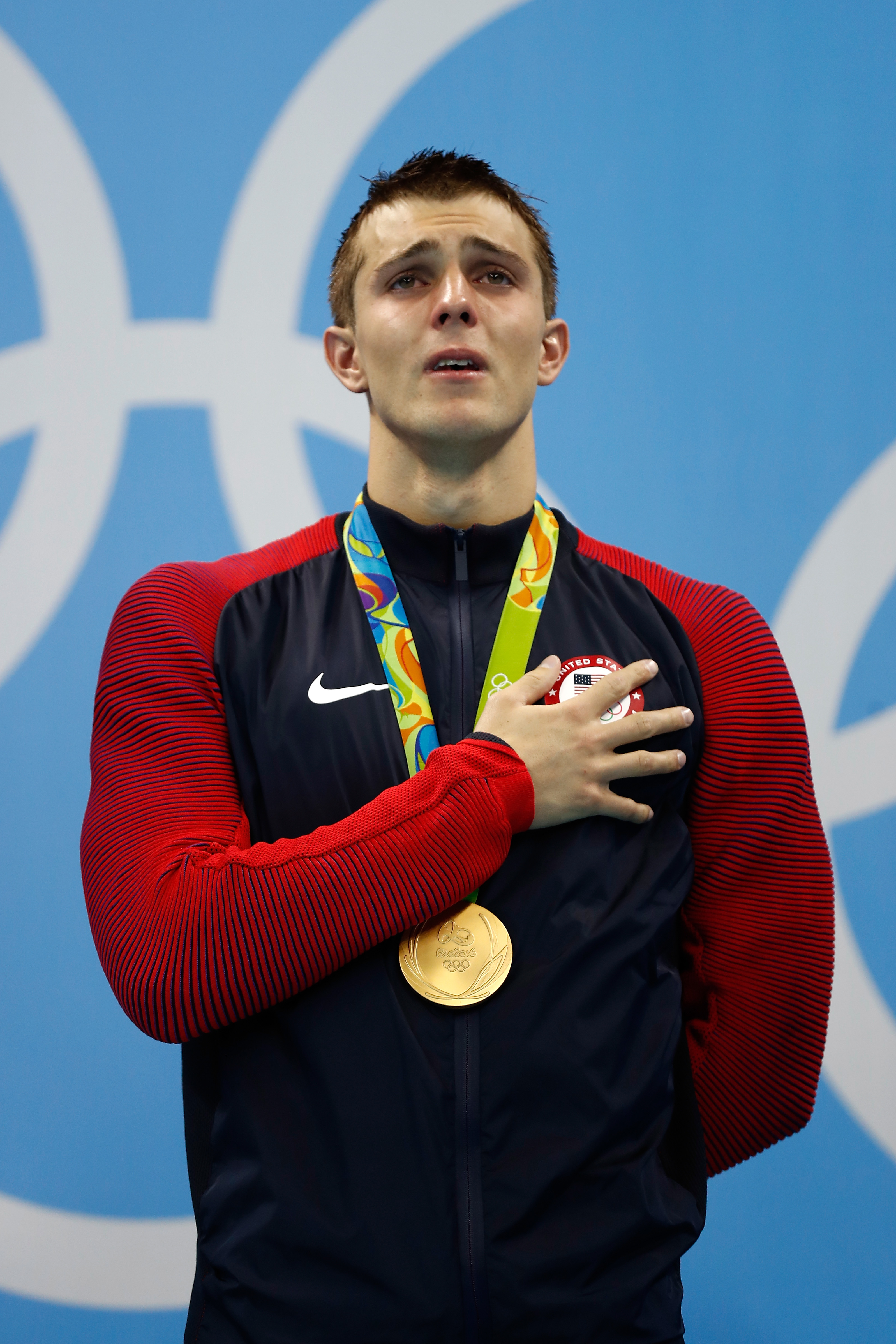 Ryan Held stands with gold medal around their neck, holding hand over heart during national anthem at the Olympics