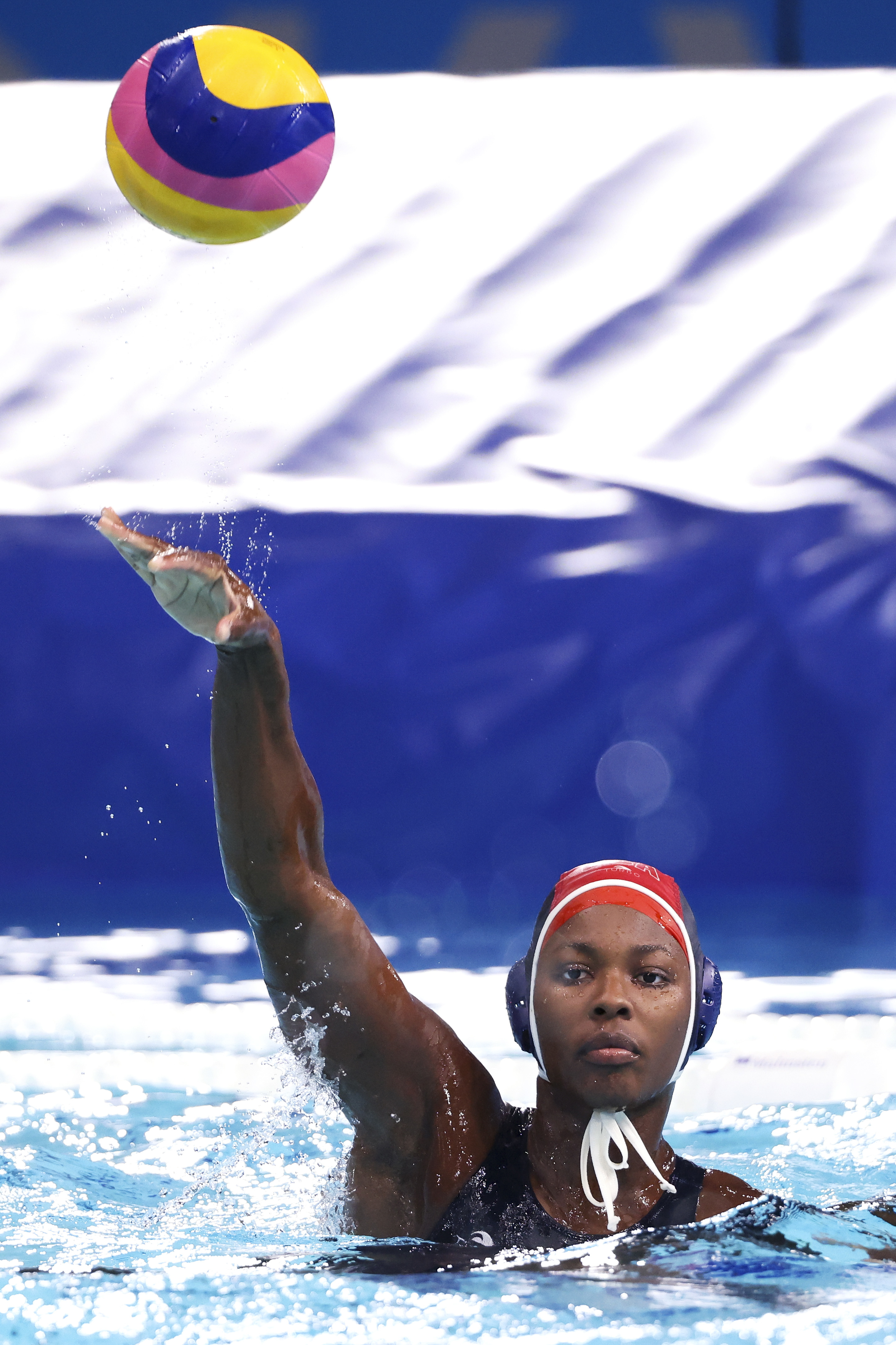 Ashleigh Johnson wearing a red cap and blue swimsuit throws the ball during a game