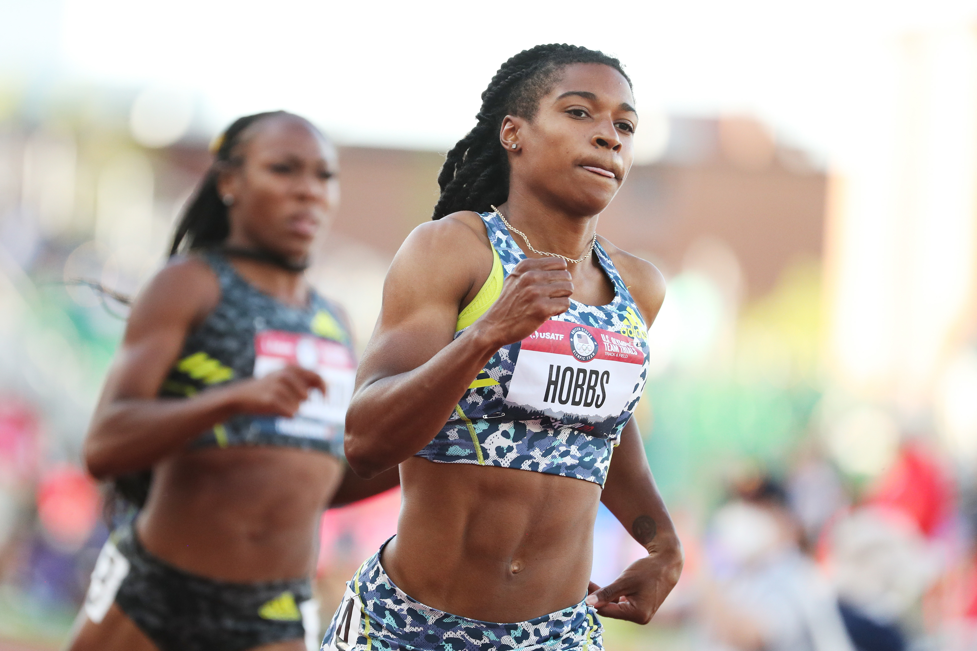 Aleia Hobbs in action during a track race, leading another competitor. Both athletes focus intensely on their performance in a stadium setting