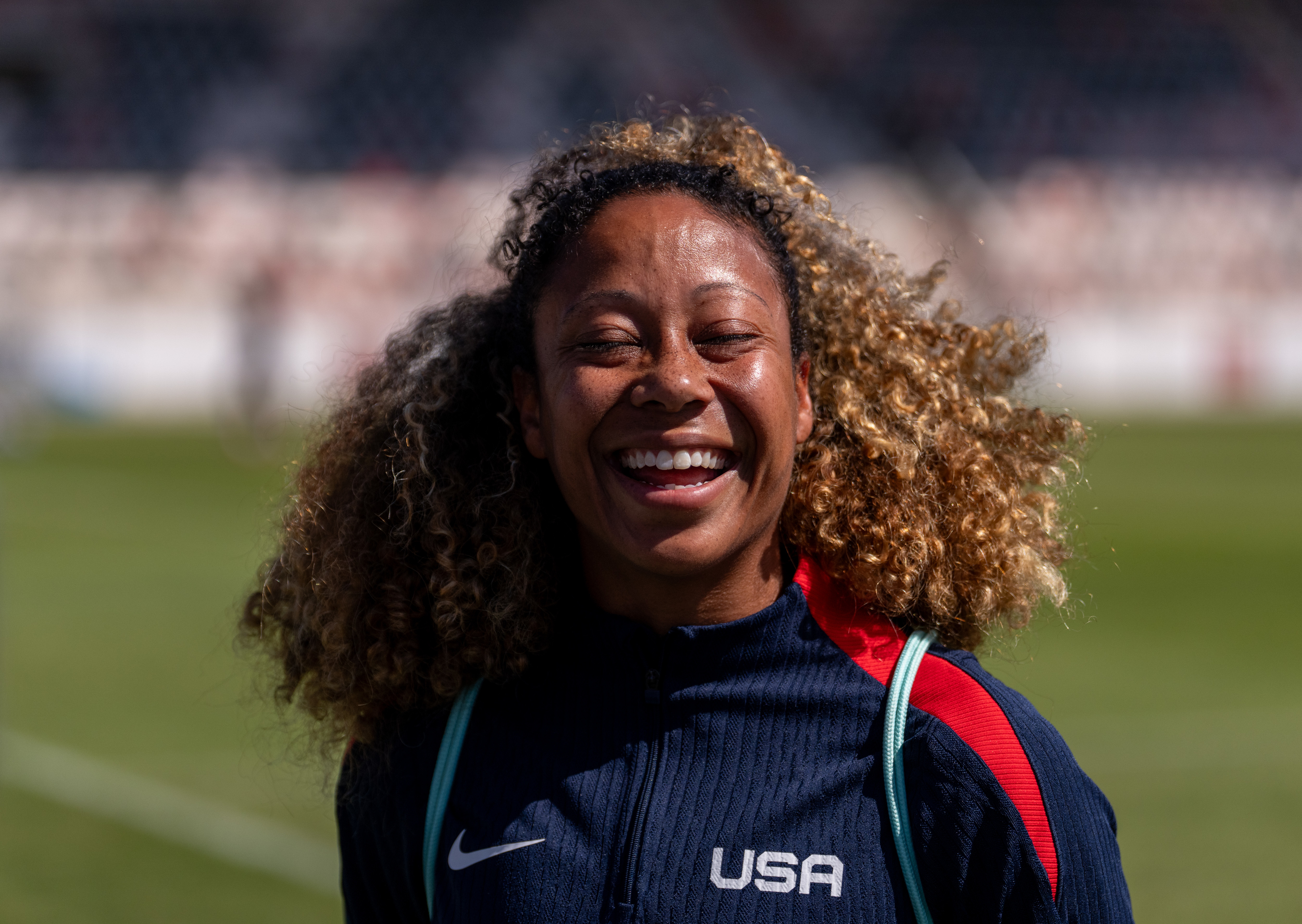 Casey Krueger wearing a USA tracksuit, is smiling widely on a sports field