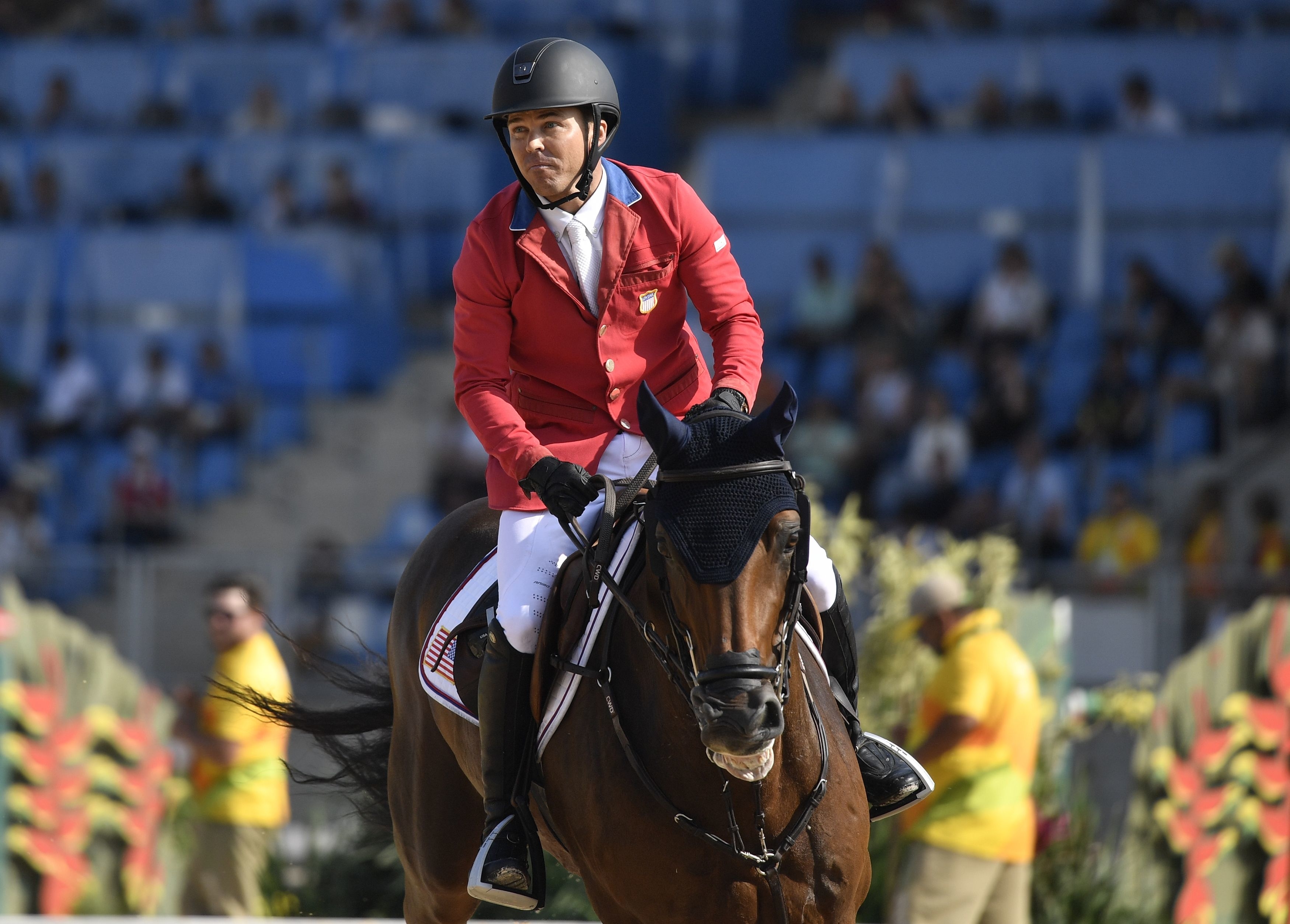 Equestrian rider wearing a helmet and red jacket riding a horse in a show jumping competition event
