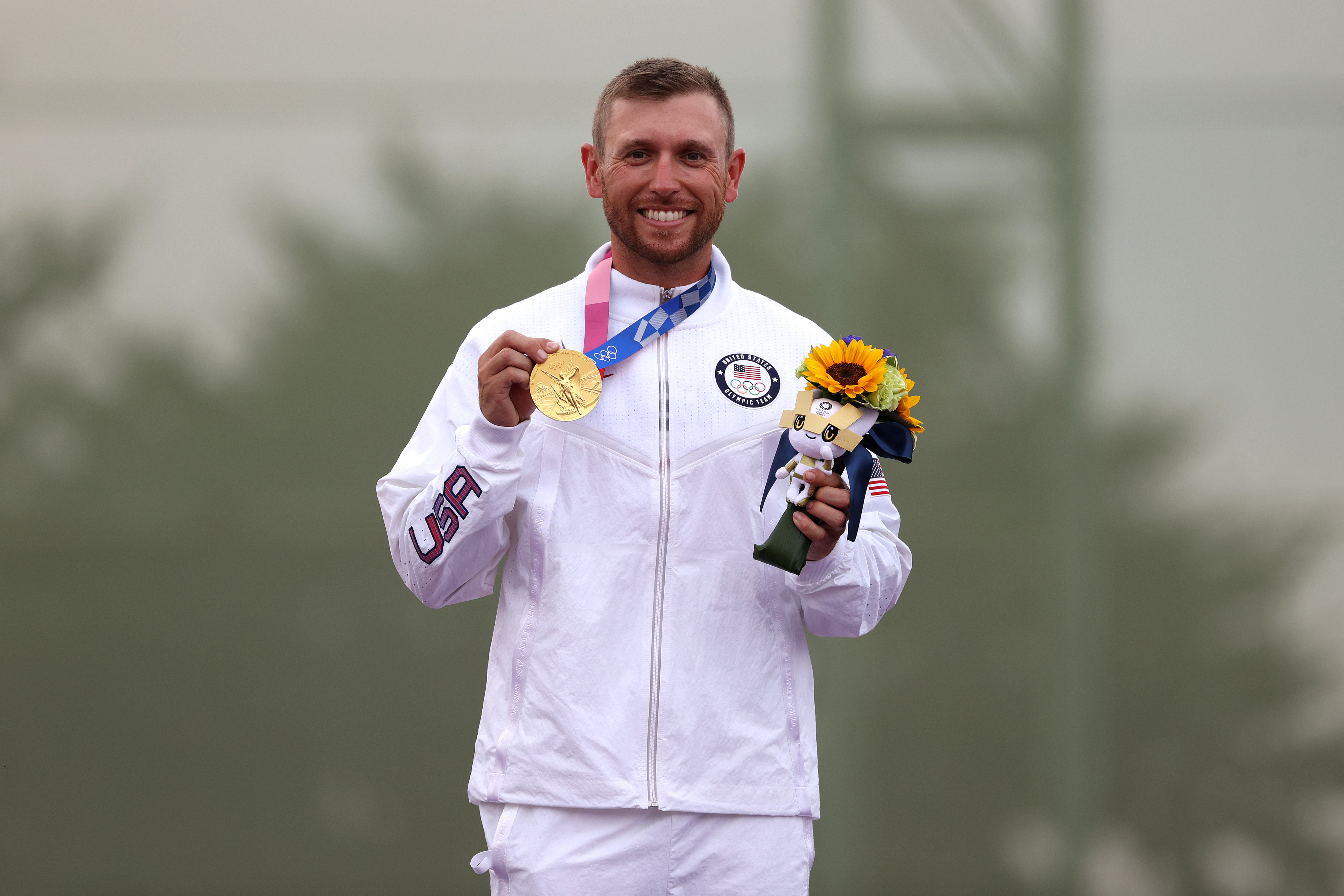 Athlete in white USA tracksuit holding a gold medal and a bouquet of sunflowers, smiling