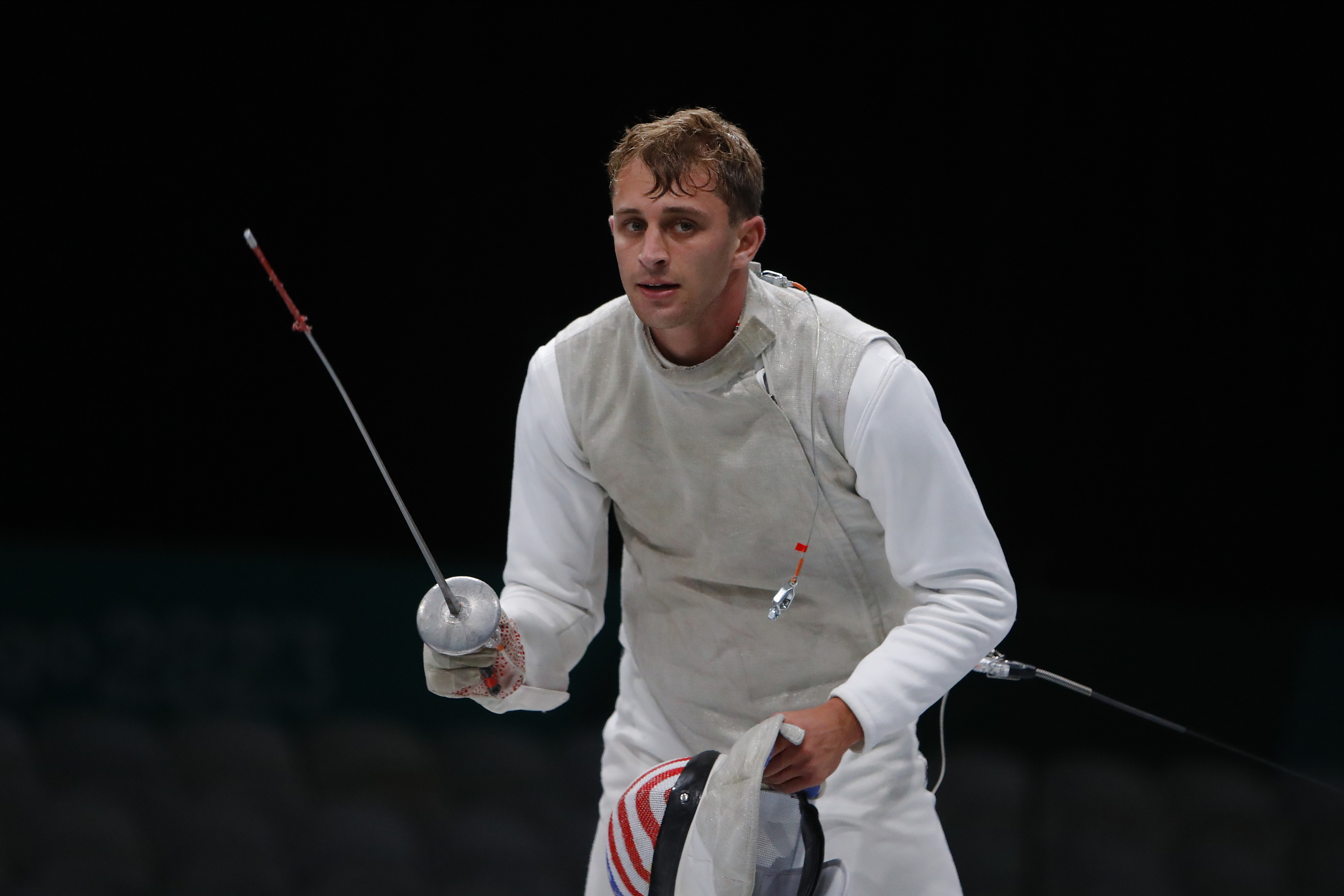 Fencer Nick Itkin holding foil and headgear during a match