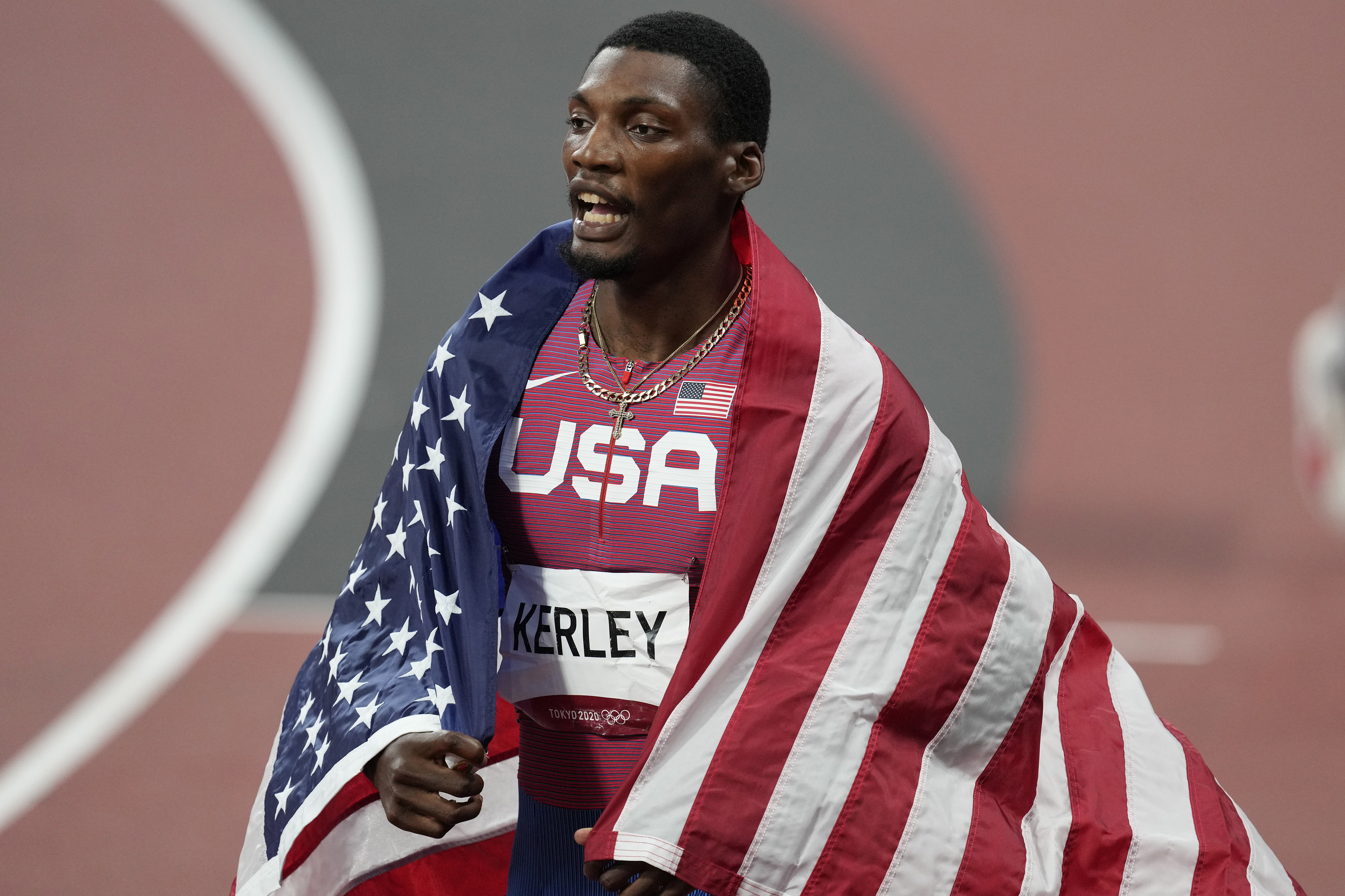 Athlete Fred Kerley, draped in an American flag, celebrates after a race, wearing a USA jersey
