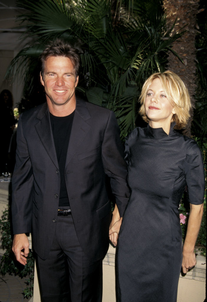 Dennis Quaid and Meg Ryan are holding hands and smiling while standing outdoors. Both are dressed in formal black attire
