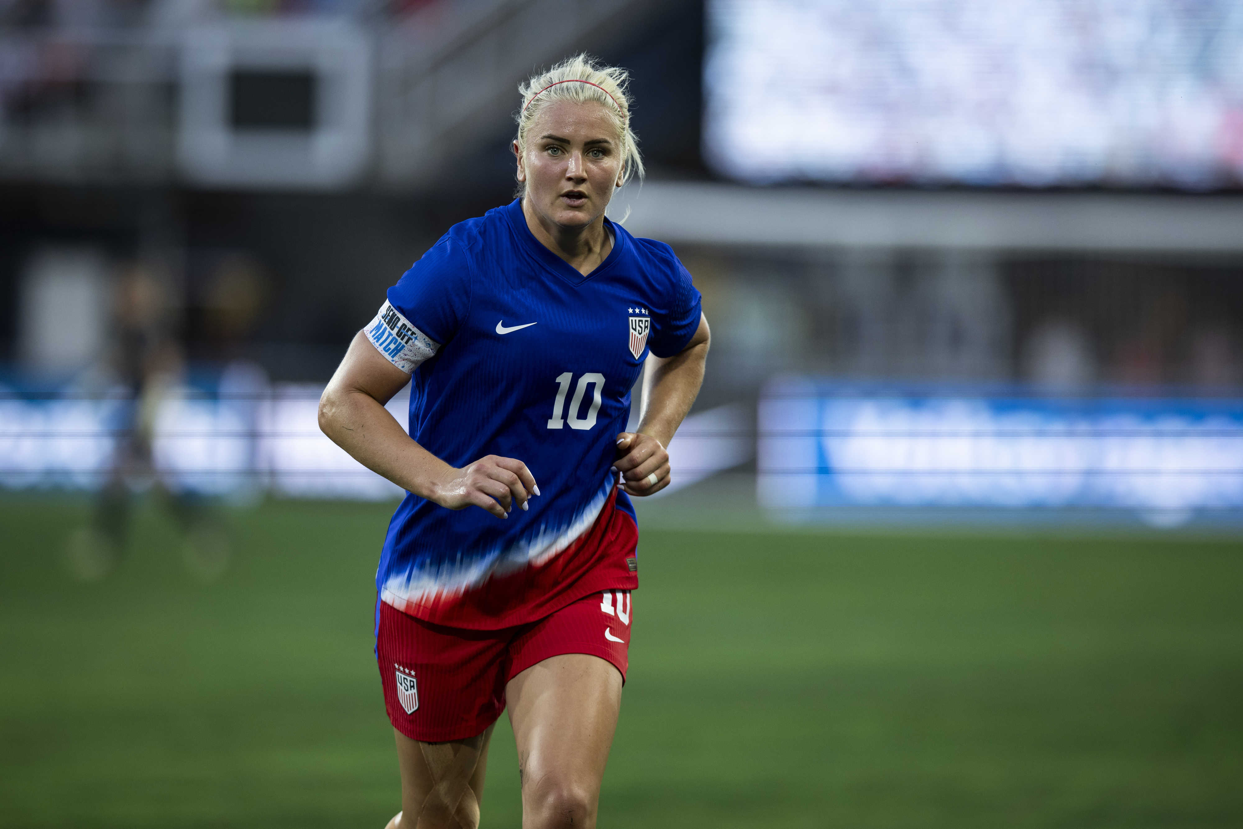 Lindsay Horan, wearing a soccer jersey and shorts, is running on the field during a game