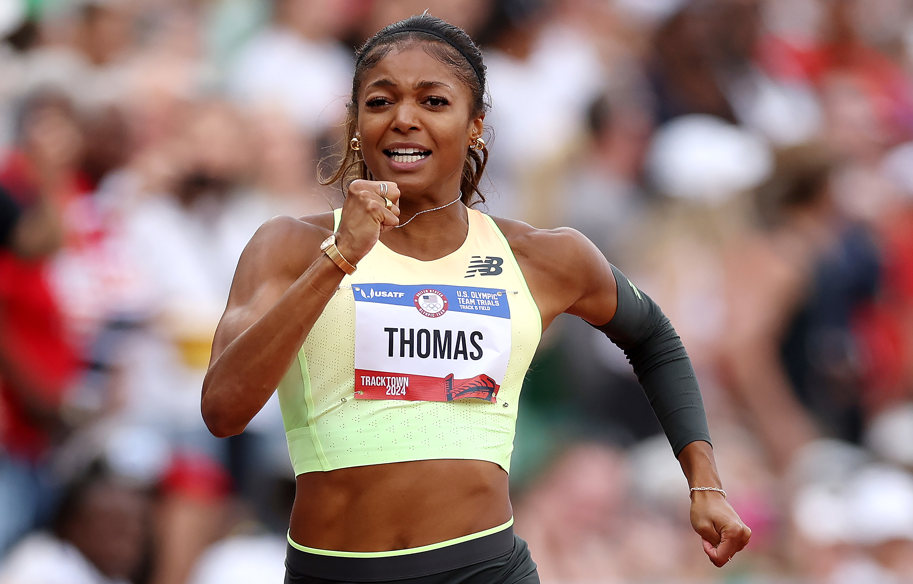 Gabby Thomas runs in a track event, wearing a sports top and bib with &quot;THOMAS&quot; printed on it. She appears focused and determined